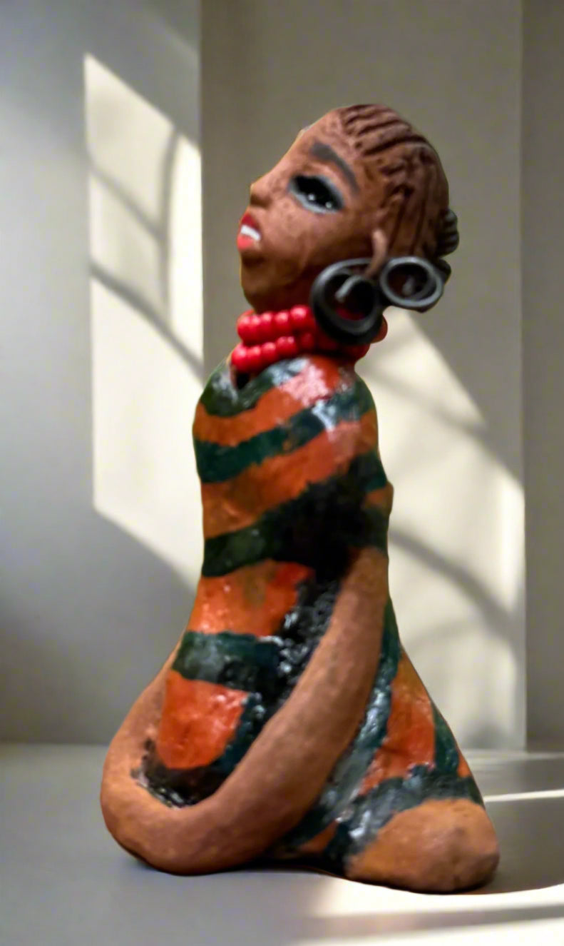 Experience the bold and fearless Shiba from the Herdew Collection! This raku fired sculpture stands tall at 5" x 3" x 3" and weighs a brave 7 ozs. Clothed in a striking orange and black dress, Shiba's coiled wire hair stretches over 1 foot. With confident outstretched arms, she strikes a yoga pose. Begin your collection with the captivating Kitty and embrace adventure!