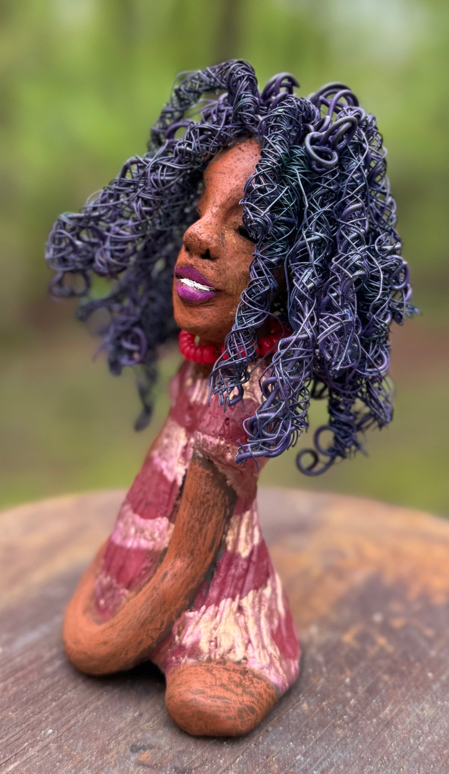 Introducing LaDonya, who measures 8" x 4. 5" x 5.5" and weighs 1.27 lbs. Her beauty is adorned with a lovely honey brown complexion, soft dark red lips, and long twisted purple locs that cascade down to her waist. Her metallic striped copper gold glazed dress adds a luxurious touch. With over 75 feet of 16 and 24 gauge wire for hair, it took over 6 hours to perfect her twisted hairstyle. Her hopeful expression and captivating eyes make her the perfect addition to any home. Plus, enjoy free shipping with our
