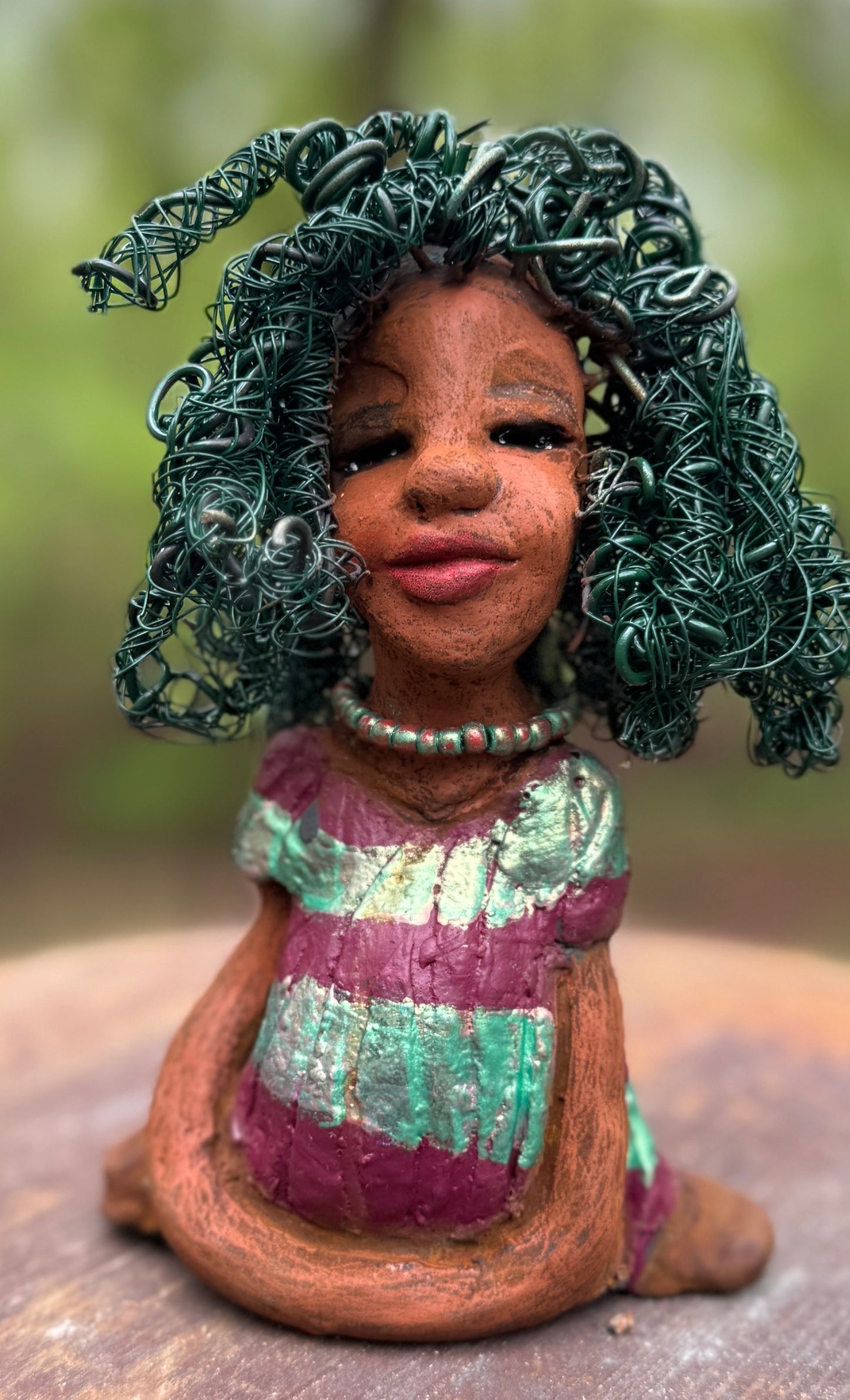 Coco is a 7.5" x 4" x 3" figurine that weighs 1 lb and wears a stunning red and green dress with stripes. Her wire hair is intricately coiled and adds to her regal appearance. Poised in a yoga pose, Coco's expression exudes curiosity, making her a perfect addition to the Herdew Collection.