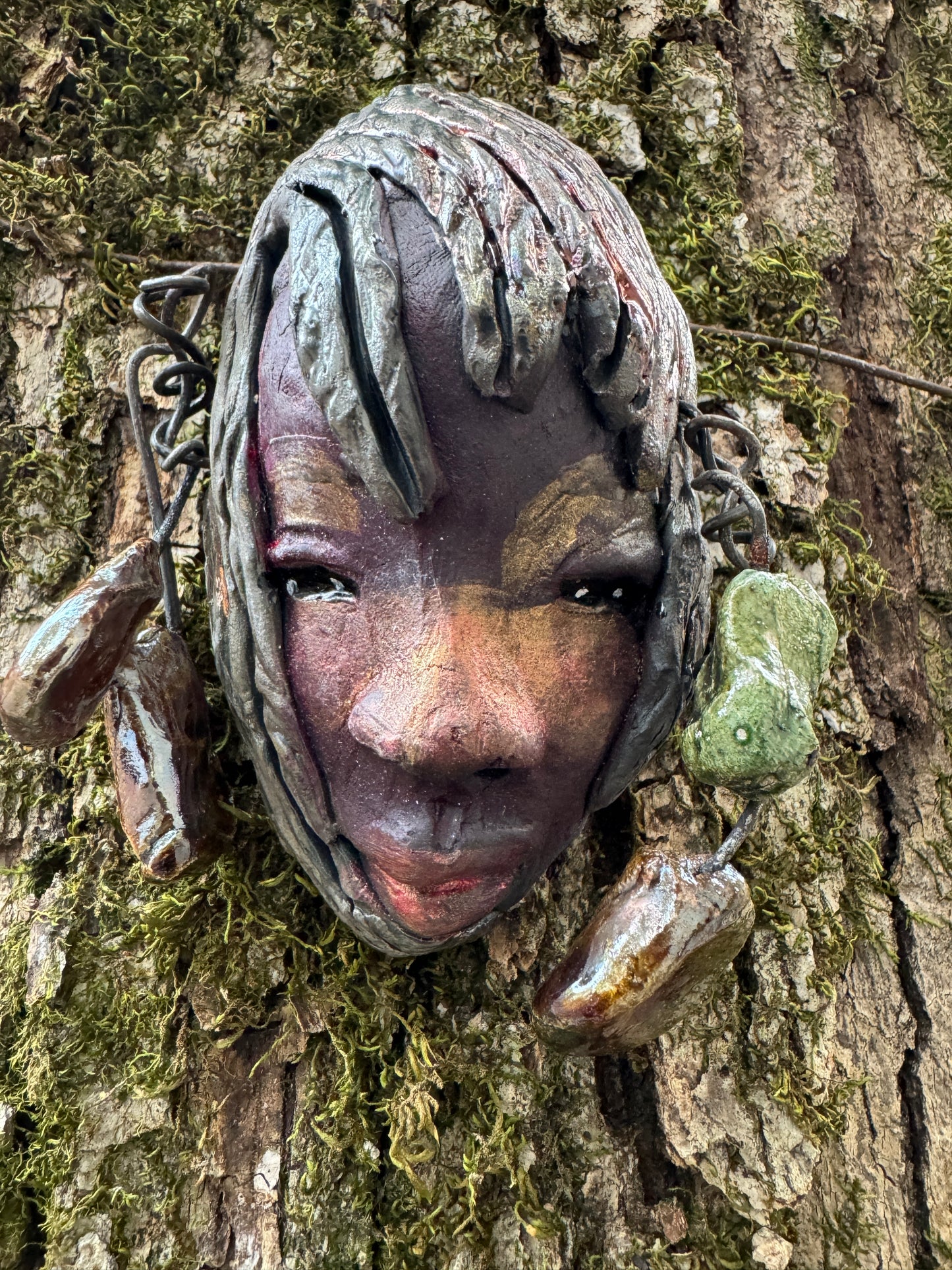 Monroe is 4" x 5" and weighs 8 oz. It is a Raku fired mask crafted from mixed media, with hand-crafted beads and over 15' of 16 and 24 gauge wire used in its "hair". Whether inside or outdoors, it can be the perfect decoration for your home; the photo of Monroe was taken on a tree.