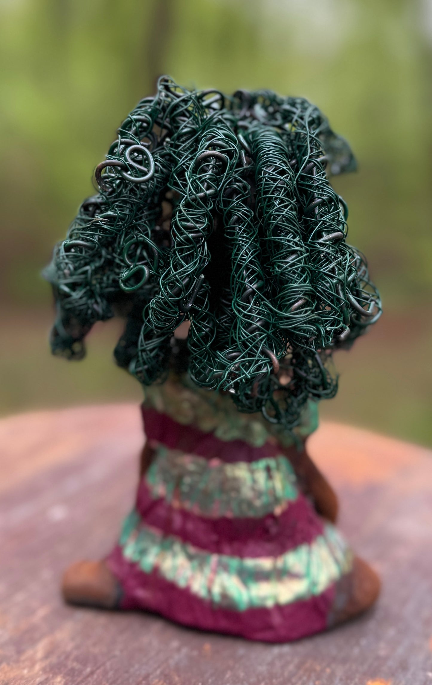 Coco is a 7.5" x 4" x 3" figurine that weighs 1 lb and wears a stunning red and green dress with stripes. Her wire hair is intricately coiled and adds to her regal appearance. Poised in a yoga pose, Coco's expression exudes curiosity, making her a perfect addition to the Herdew Collection.