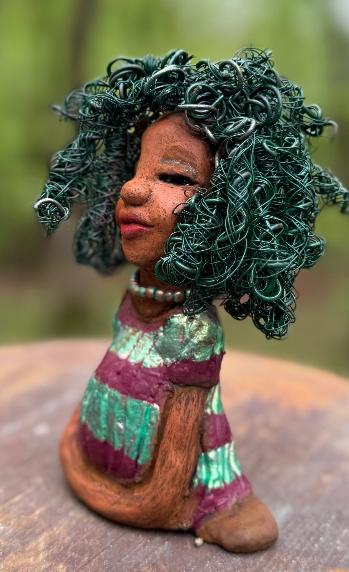 Coco is a 7.5" x 4" x 3" figurine that weighs 1 lb and wears a stunning red and green dress with stripes. Her wire hair is intricately coiled and adds to her regal appearance. Poised in a yoga pose, Coco's expression exudes curiosity, making her a perfect addition to the Herdew Collection.
