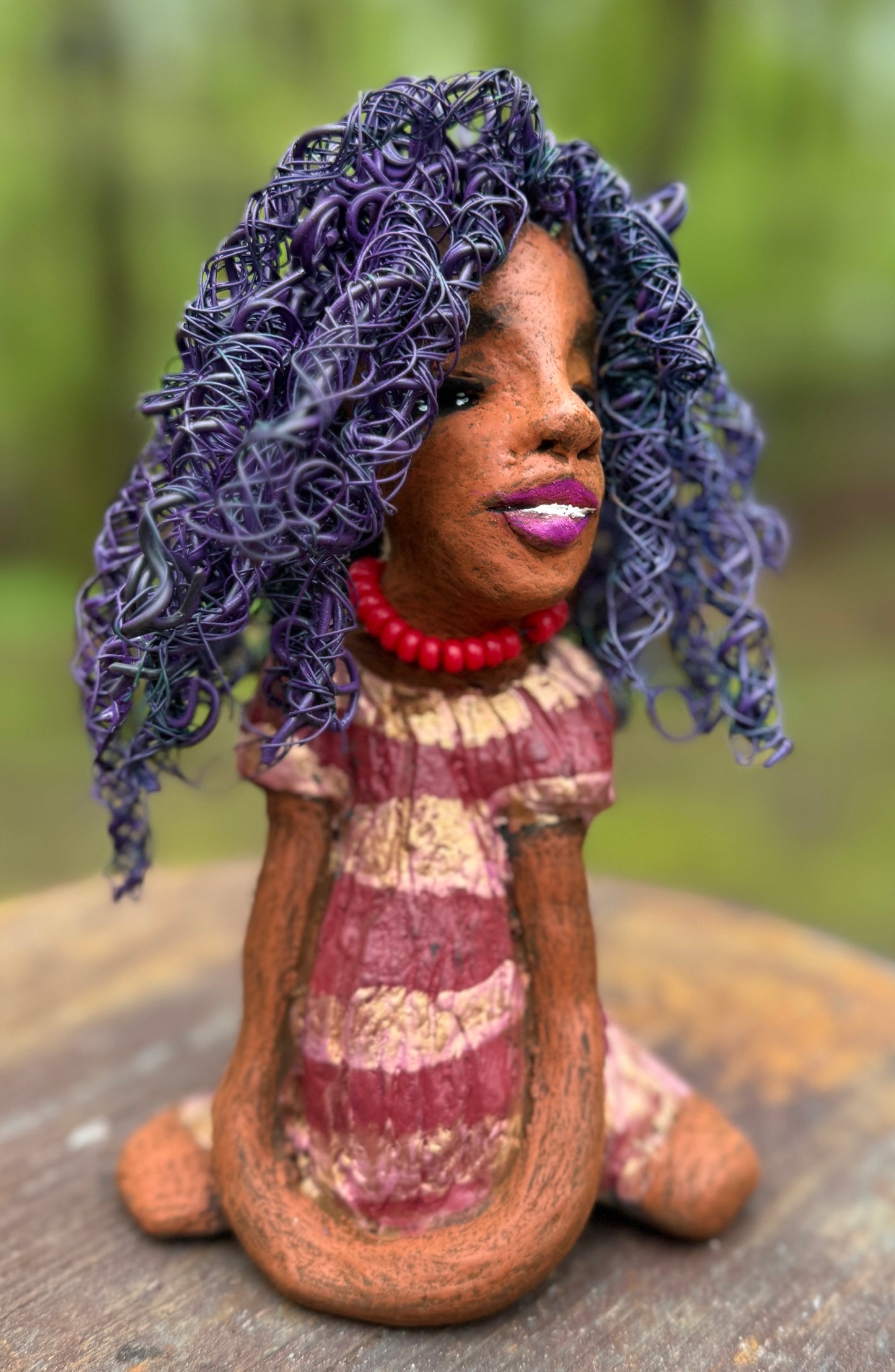 Introducing LaDonya, who measures 8" x 4. 5" x 5.5" and weighs 1.27 lbs. Her beauty is adorned with a lovely honey brown complexion, soft dark red lips, and long twisted purple locs that cascade down to her waist. Her metallic striped copper gold glazed dress adds a luxurious touch. With over 75 feet of 16 and 24 gauge wire for hair, it took over 6 hours to perfect her twisted hairstyle. Her hopeful expression and captivating eyes make her the perfect addition to any home. Plus, enjoy free shipping with our