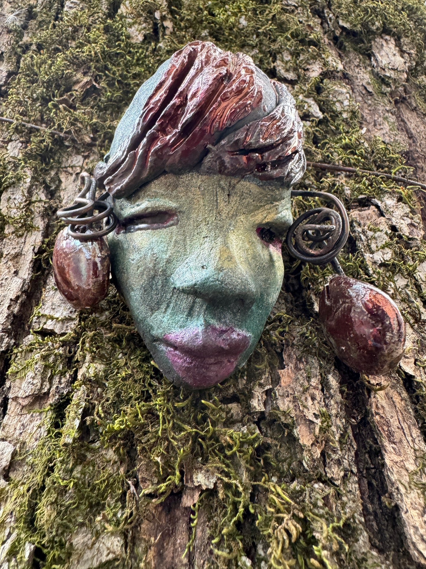 Monday weighs 3.2 oz and measures 3" by 4" in diameter. Her hair is copper-braided and her complexion is a light blueish green hue with purple lips. She is an ideal introductory piece from the HerDew mask collection.