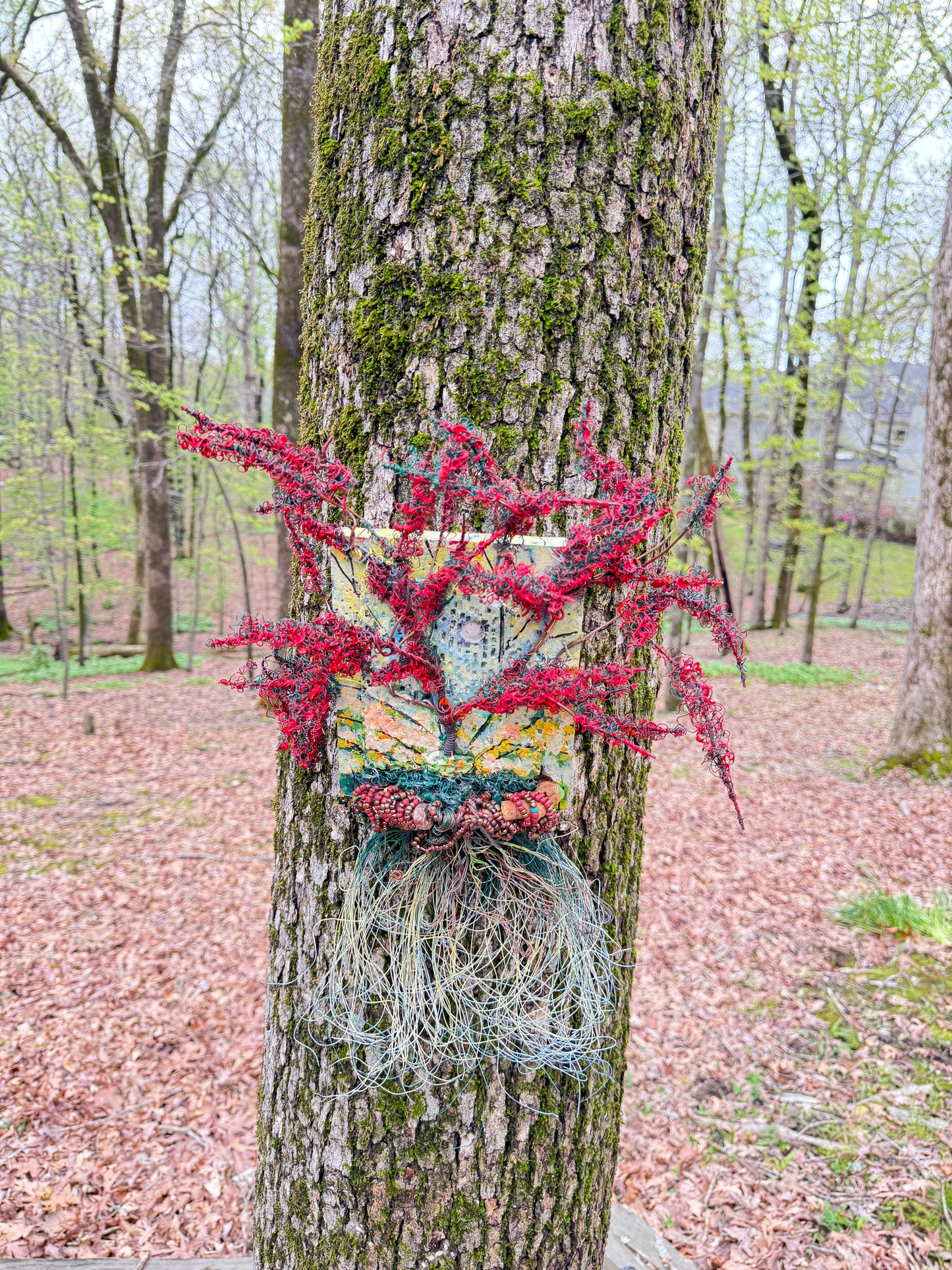 Chrisom Crown is a unique mixed media landscape, measuring 17 inches in height and 15 inches in width. The piece features a combination of 16 and 24 gauge wire, along with handmade Raku fire beads. It also includes a RAKU fired and hand painted texture tile mounted on a 7" x 5" wood base. The sun peeks through the vibrant Crimson leaves, creating the illusion of a warm summer day.