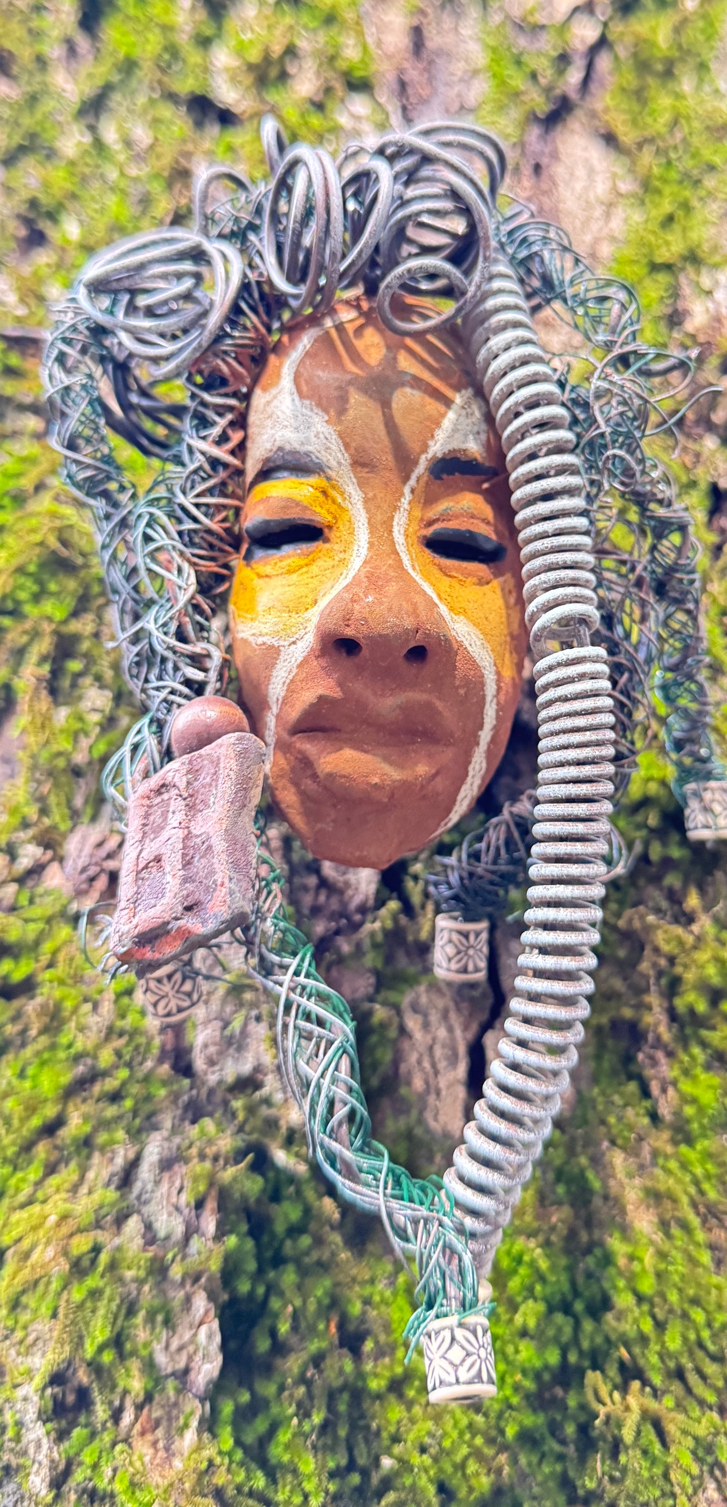 This eye-catching raku fired mask named Mitchell adds a unique touch to any collection, measuring 4” x 6” and weighing 6oz. It features 25 feet of 24 and 16 gauge wire and a three-colored complexion, all captured in stunning photography on a tree. To complete the look, the piece comes with two large Raku fired earrings with wooden beads. Don't hesitate to add Mitchell to your HerDew collection.