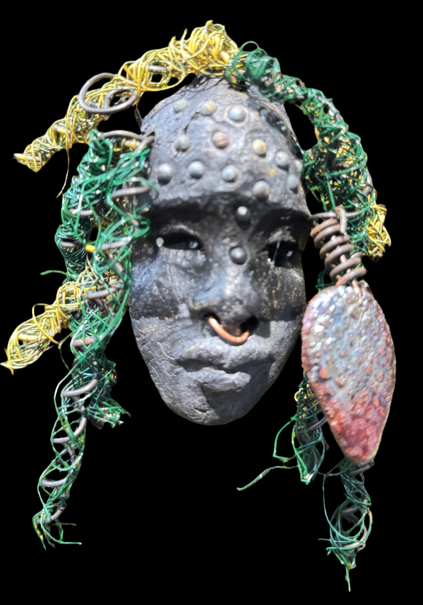 Enhance your HerDew mask collection with Kao! This mixed media raku fire mask is 4” x 6” and 6oz., featuring 25 feet of 24 and 16 gauge wire and a copper nose ring. Its exotic appeal is captured in a photo on tree bark, adding a unique touch to your collection. The mask's Smokey black complexion and Raku fired earring with a wooden bead make it a truly stunning piece..