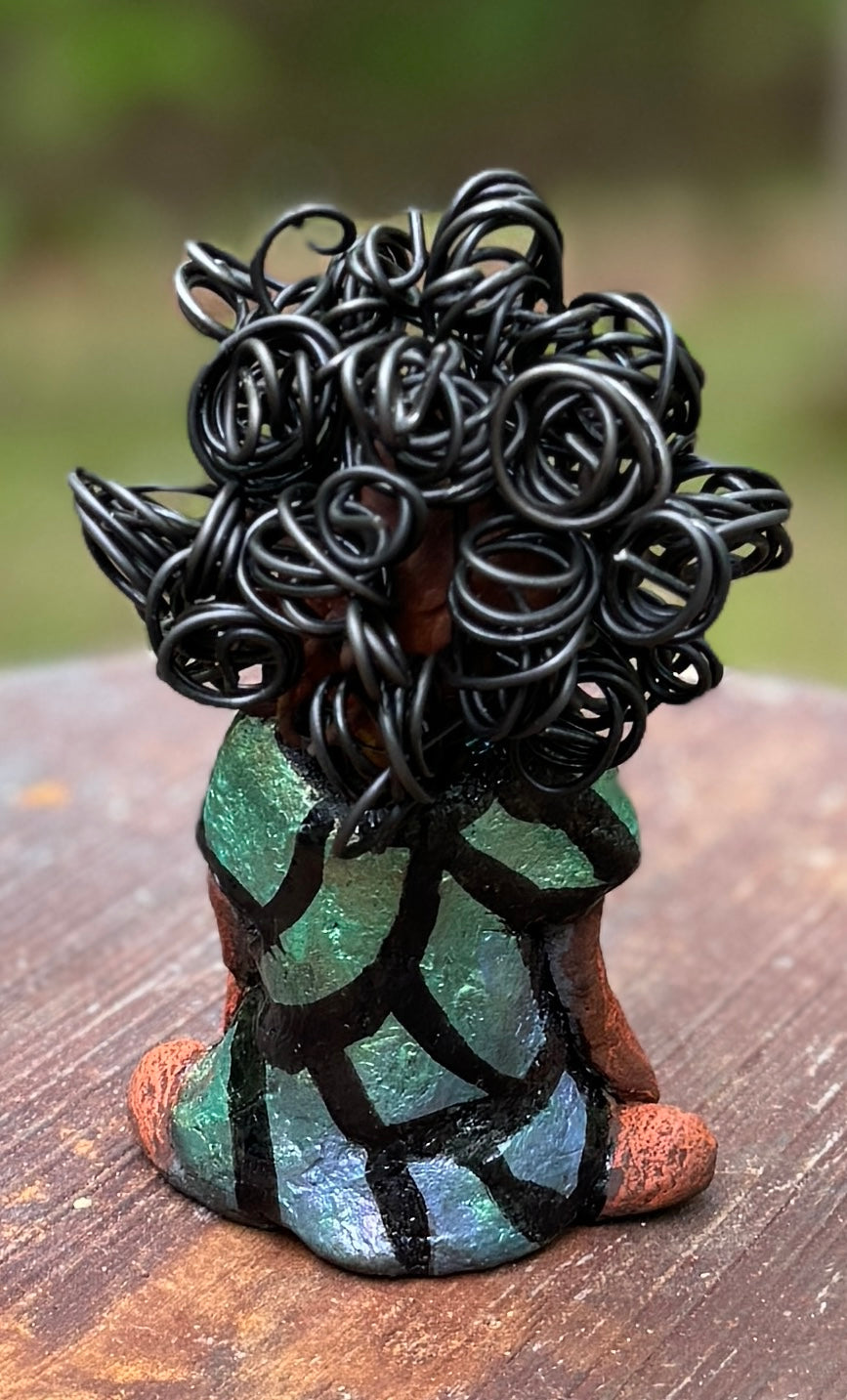 Discover Taci, the bold figurine standing at 5.5" tall and weighing only 8.6 ozs, adorned in a striking black and green African print dress. With her hair styled in coils and her hands calmly resting in a yoga pose, Taci emanates confidence. Join the Herdew Collection and embark on an exciting journey with our complimentary shipping and customer-friendly return policy. Don't hesitate to claim this unique treasure!