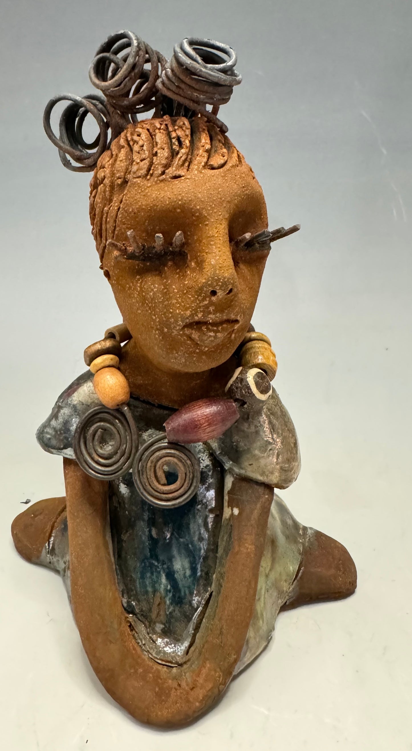 Introducing Kitty, the fearless one standing at 6" x 4" x 3" and weighing 12 ozs! Adorned in a stunning metallic gold dress, Kitty's coiled wire hair measures over 3 feet. Poised in a yoga pose, her long arms rest confidently at her lap. Start your collection off strong with the captivating Kitty from the Herdew Collection