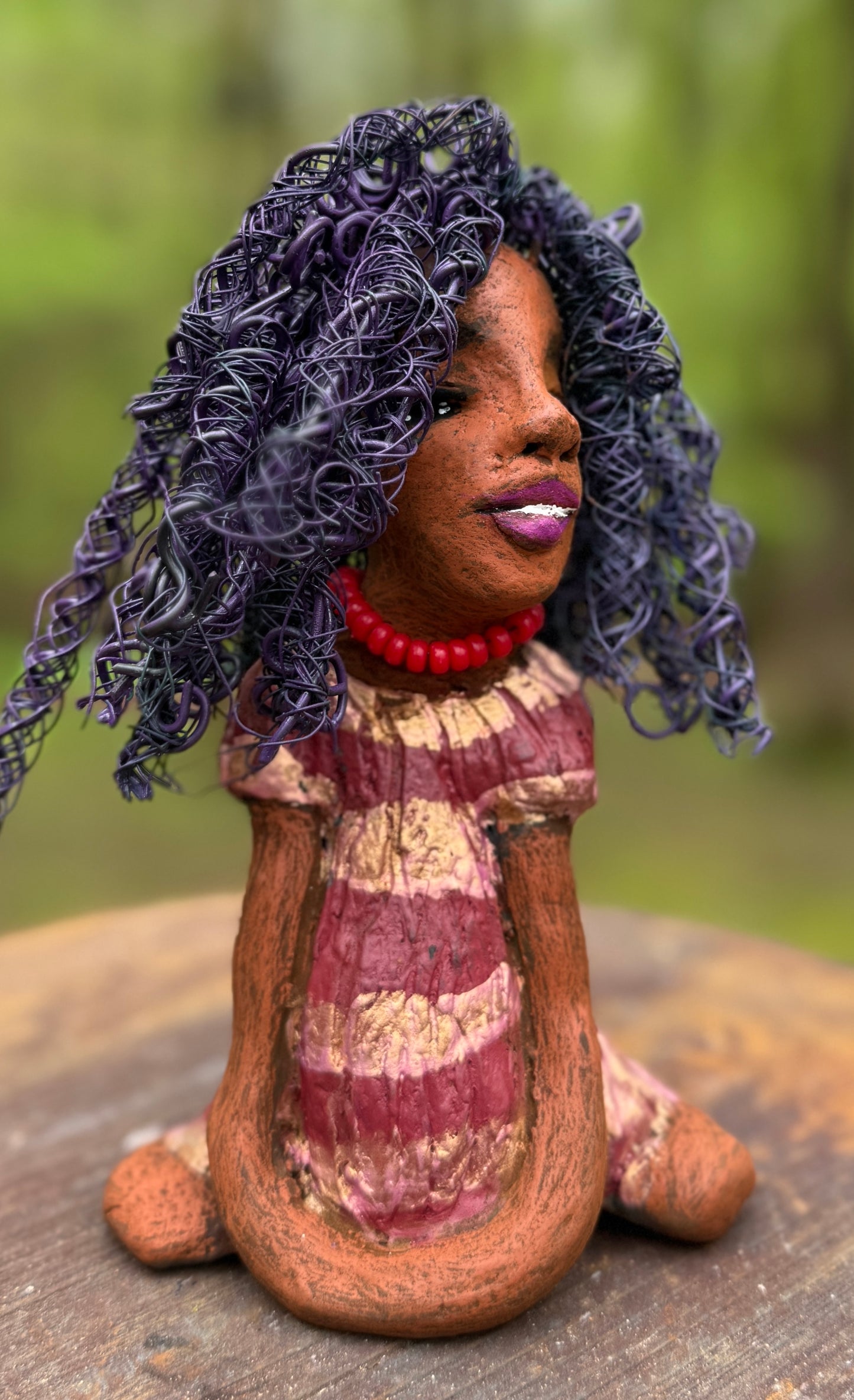 Introducing LaDonya, who measures 8" x 4. 5" x 5.5" and weighs 1.27 lbs. Her beauty is adorned with a lovely honey brown complexion, soft dark red lips, and long twisted purple locs that cascade down to her waist. Her metallic striped copper gold glazed dress adds a luxurious touch. With over 75 feet of 16 and 24 gauge wire for hair, it took over 6 hours to perfect her twisted hairstyle. Her hopeful expression and captivating eyes make her the perfect addition to any home. Plus, enjoy free shipping with our