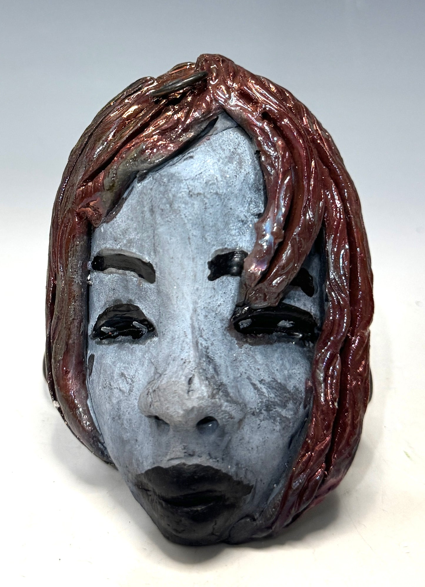 Mia weighs 4 oz and measures 4" by 3" in diameter. Her hair is copper-braided and her complexion is a light grayish blue hue with black lips. She is an ideal introductory piece from the HerDew mask collection.