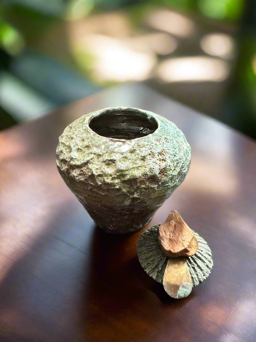 Discover the intricate qualities of this earthy alligator green textured lidded pot, measuring 6 inches in height and 5 inches in width and depth with a 2-inch opening. The lid showcases a natural rock embellishment and highlights brass accents. The opening measures 2 inches by 0.5 inches.