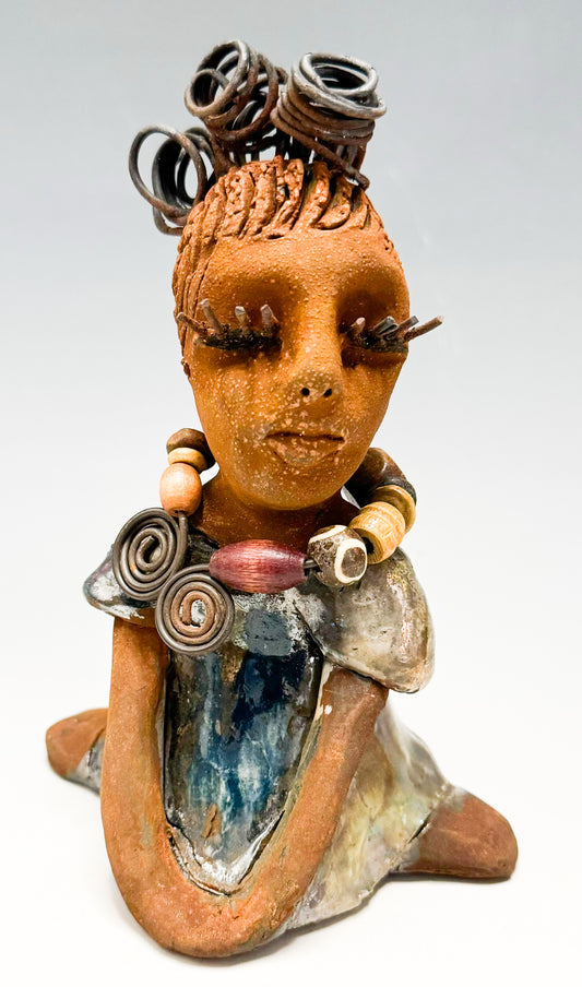 Introducing Kitty, the fearless one standing at 6" x 4" x 3" and weighing 12 ozs! Adorned in a stunning metallic gold dress, Kitty's coiled wire hair measures over 3 feet. Poised in a yoga pose, her long arms rest confidently at her lap. Start your collection off strong with the captivating Kitty from the Herdew Collection