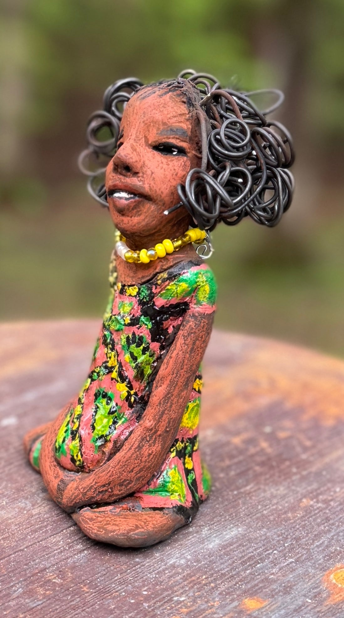 Introducing Katie, the fearless figurine who measures 6" x 4" x 3" and weighs a mere 11 ozs. Donning a stunning speckled red and green dress and with her coiled hair as her crown of glory, Katie exudes confidence and courage as she sits in a yoga pose, exuding curiosity. Begin your journey with the Herdew Collection and experience the thrill of free shipping and our customer-friendly return policy. Don't miss out on this one-of-a-kind piece!