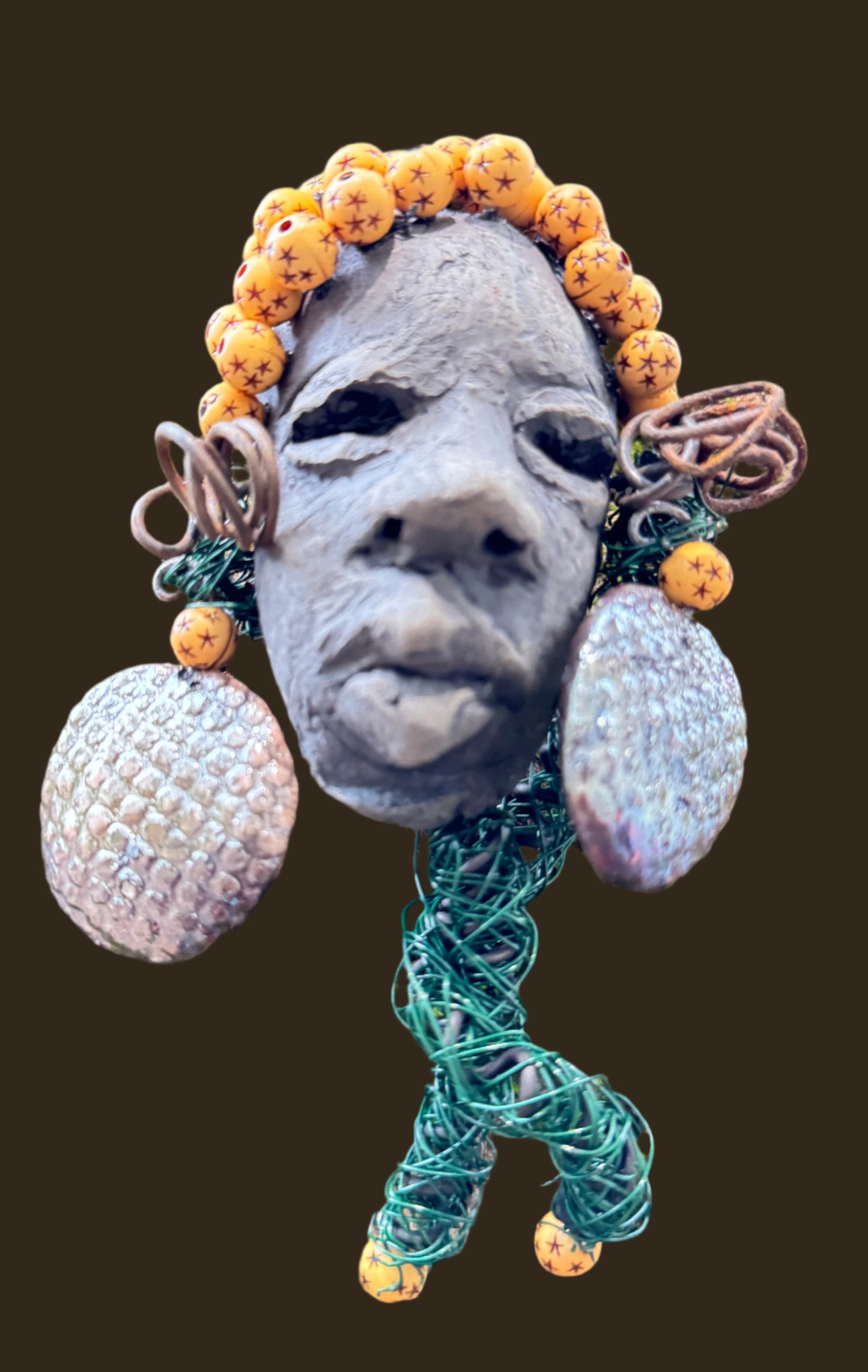Introducing Cali, a 3” x 5” 5oz. mixed media raku fire mask adorned with a copper nose ring, three-colored complexion, and two large Raku fired earrings with a wooden bead. With 15 feet of 24 and 16 gauge wire, this piece is a stunning addition to your HerDew mask collection. See the beautiful Cali against a tree bark background.