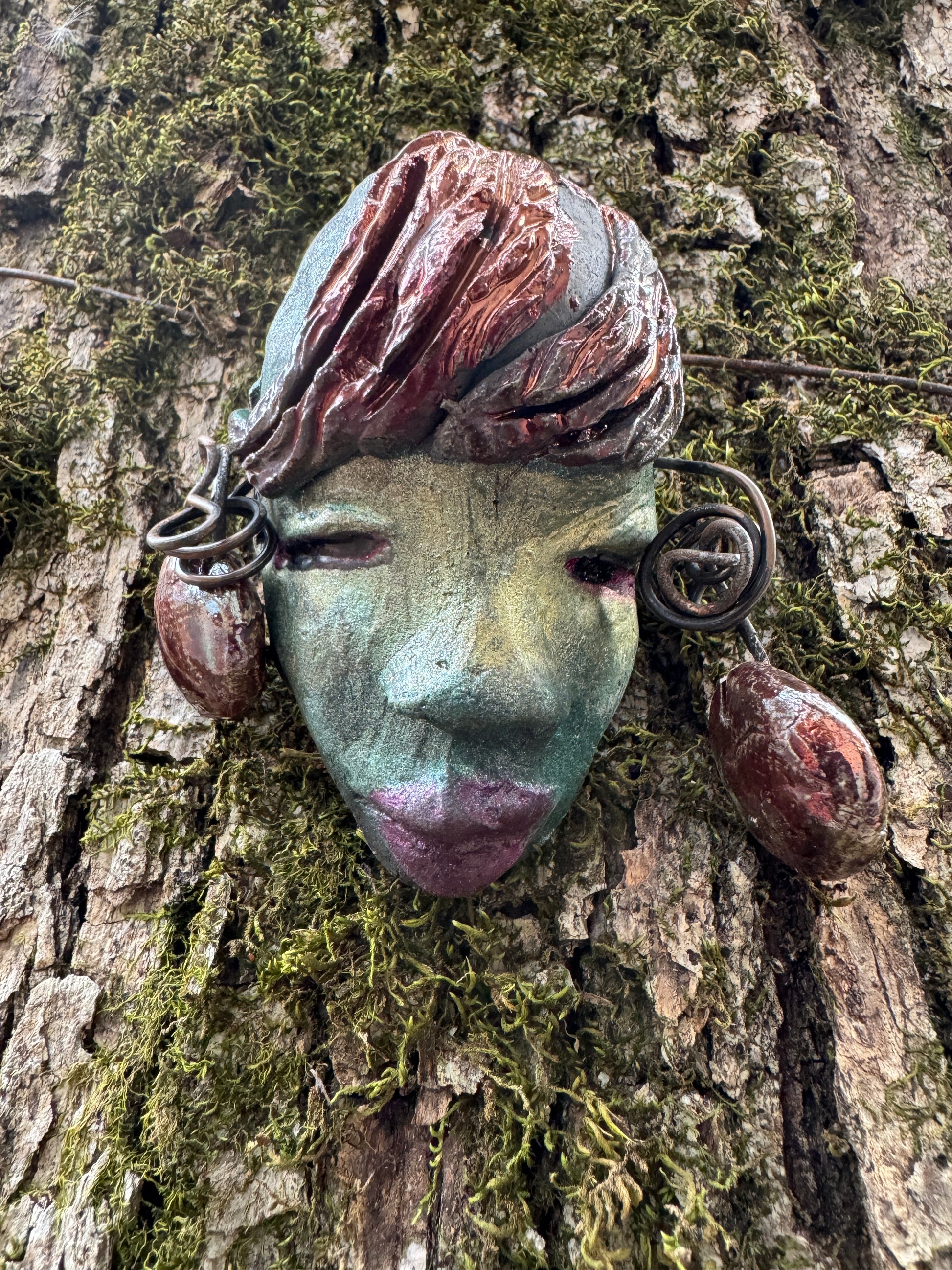 Monday weighs 3.2 oz and measures 3" by 4" in diameter. Her hair is copper-braided and her complexion is a light blueish green hue with purple lips. She is an ideal introductory piece from the HerDew mask collection.