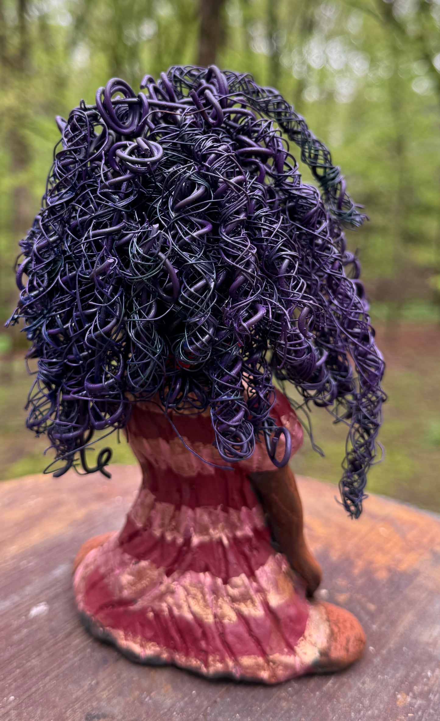 Introducing LaDonya, who measures 8" x 4. 5" x 5.5" and weighs 1.27 lbs. Her beauty is adorned with a lovely honey brown complexion, soft dark red lips, and long twisted purple locs that cascade down to her waist. Her metallic striped copper gold glazed dress adds a luxurious touch. With over 75 feet of 16 and 24 gauge wire for hair, it took over 6 hours to perfect her twisted hairstyle. Her hopeful expression and captivating eyes make her the perfect addition to any home. Plus, enjoy free shipping with our