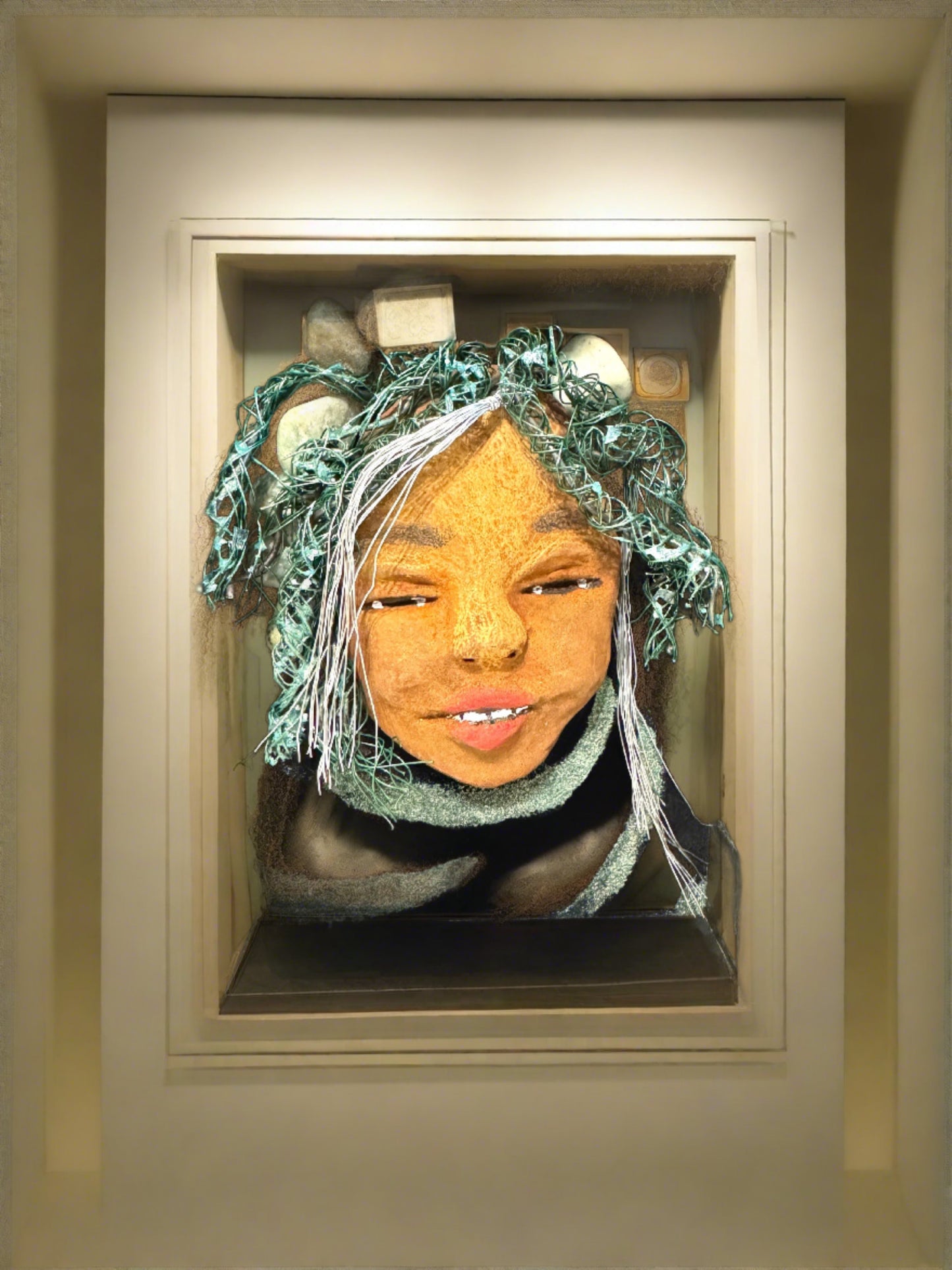 Introducing Brandie, a mixed media sculptured raku fired mask. Her features include a two-tone honey brown complexion, Ruby red lips, and hair intricately intertwined with 16 and 24 gauge wire. She is mounted on a hand-painted canvas, accented by an black landscape background, and enclosed in a 5“ x 7“ black shadowbox.
