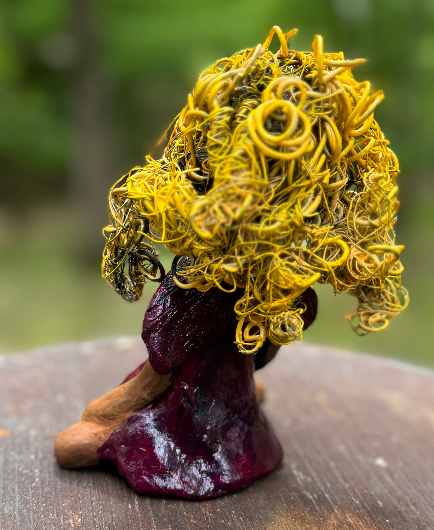 Kerri measures 6" x 4" x 3" and weighs 14ozs. She dons a stunning ruby red dress, her coiled yellow wire hair serving as her crown of glory. Poised in a yoga pose, her expression reflects curiosity. She is the perfect addition to the Herdew Collection, embodying adventure and risk-taking! Enjoy free shipping and check out our return policy.