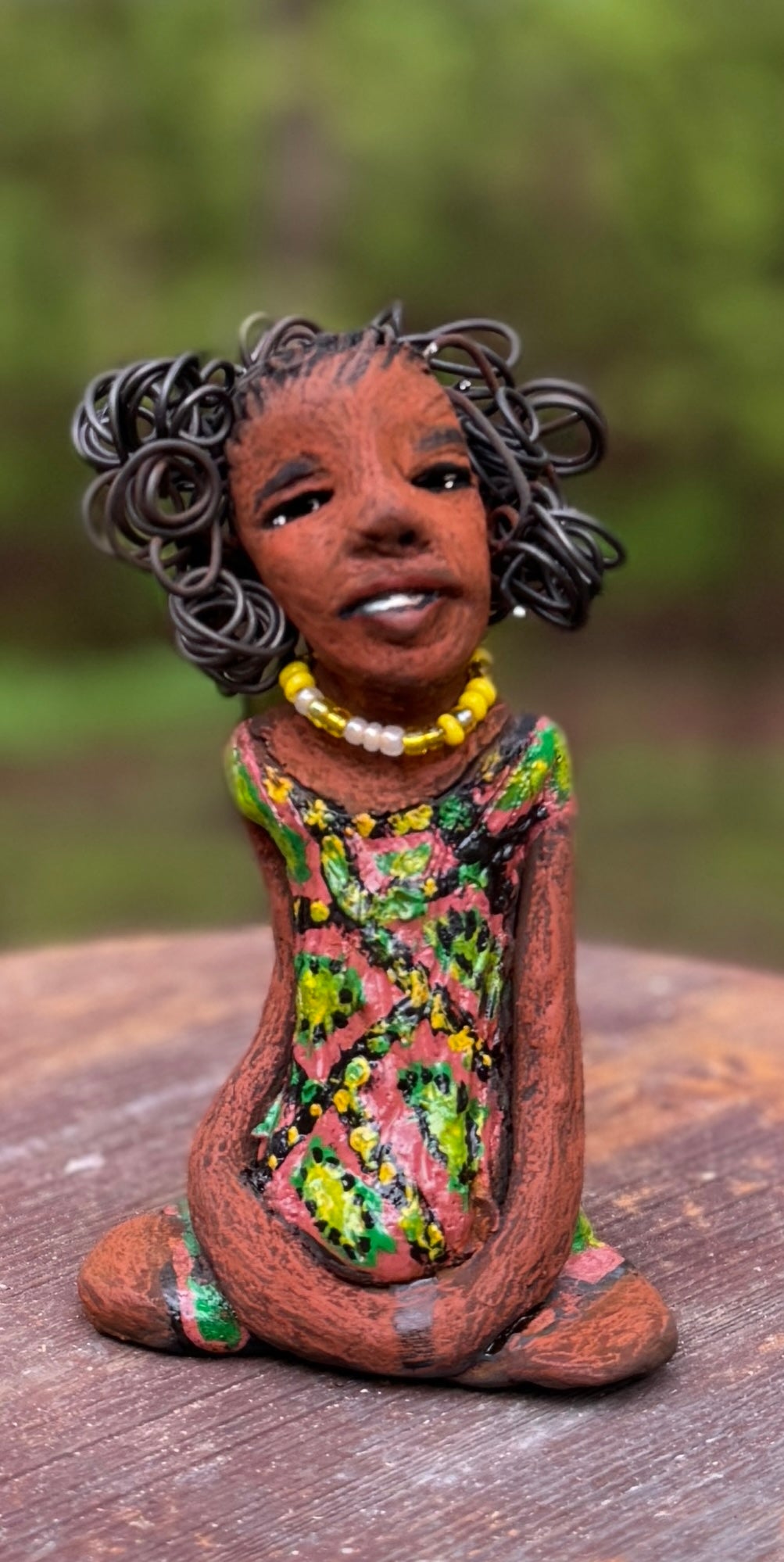 Introducing Katie, the fearless figurine who measures 6" x 4" x 3" and weighs a mere 11 ozs. Donning a stunning speckled red and green dress and with her coiled hair as her crown of glory, Katie exudes confidence and courage as she sits in a yoga pose, exuding curiosity. Begin your journey with the Herdew Collection and experience the thrill of free shipping and our customer-friendly return policy. Don't miss out on this one-of-a-kind piece!