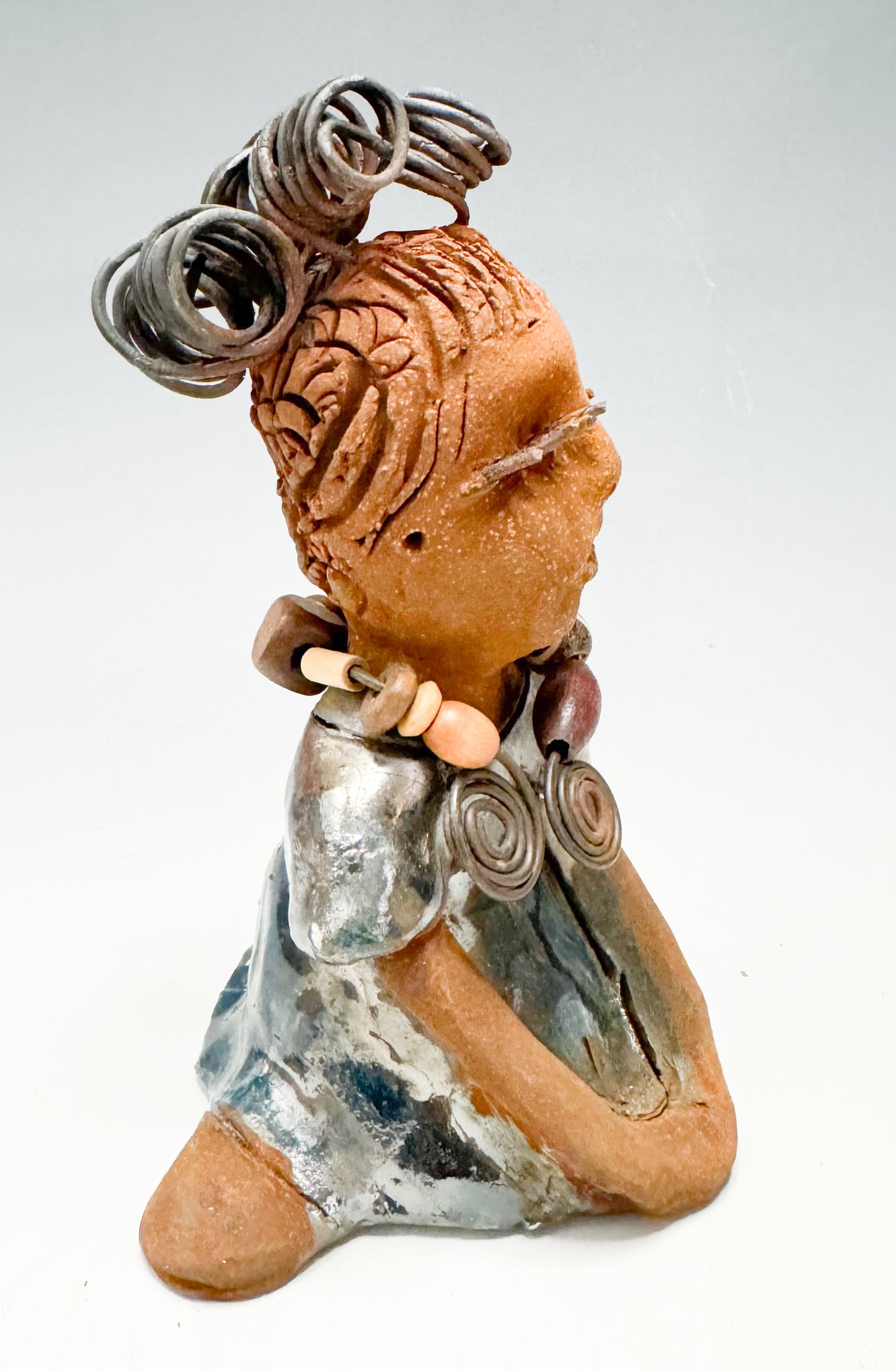 Introducing Kitty, the fearless one standing at 6" x 4" x 3" and weighing 12 ozs! Adorned in a stunning metallic gold dress, Kitty's coiled wire hair measures over 3 feet. Poised in a yoga pose, her long arms rest confidently at her lap. Start your collection off strong with the captivating Kitty from the Herdew Collection