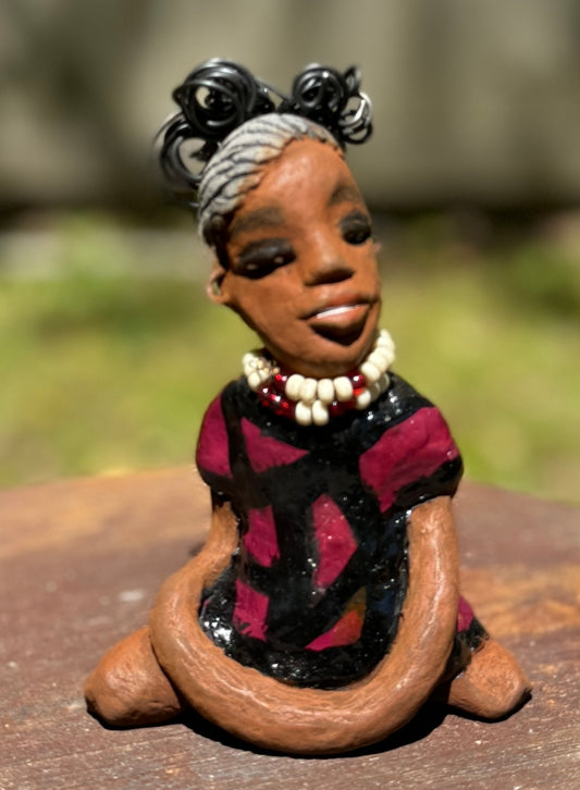 Gain a firsthand experience of the fearless Gwen from the Herdew Collection! This raku fired sculpture stands at an impressive 6" x 4" x 3" and weighs a bold 9.8 ozs. Gwen's striking striped ruby red dress and coiled wire hair, stretching over a foot, make for a captivating addition to any collection. Her confident outstretched arms and prayerful yoga pose embody a sense of adventure. Have questions? Contact us via instant messaging or chat. Check out our Shipping and Return policy.