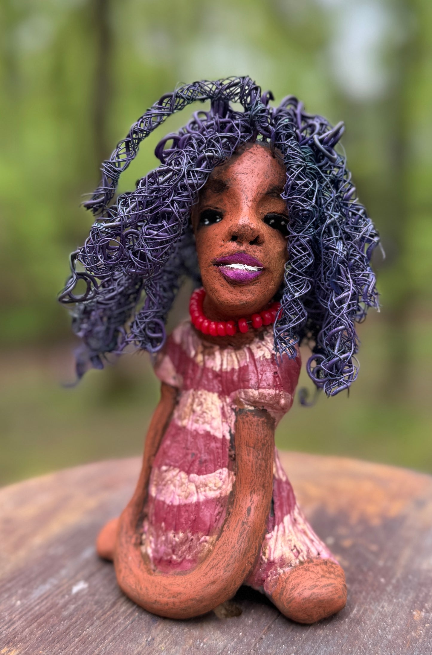 Introducing LaDonya, who measures 8" x 4. 5" x 5.5" and weighs 1.27 lbs. Her beauty is adorned with a lovely honey brown complexion, soft dark red lips, and long twisted purple locs that cascade down to her waist. Her metallic striped copper gold glazed dress adds a luxurious touch. With over 75 feet of 16 and 24 gauge wire for hair, it took over 6 hours to perfect her twisted hairstyle. Her hopeful expression and captivating eyes make her the perfect addition to any home. Plus, enjoy free shipping with our