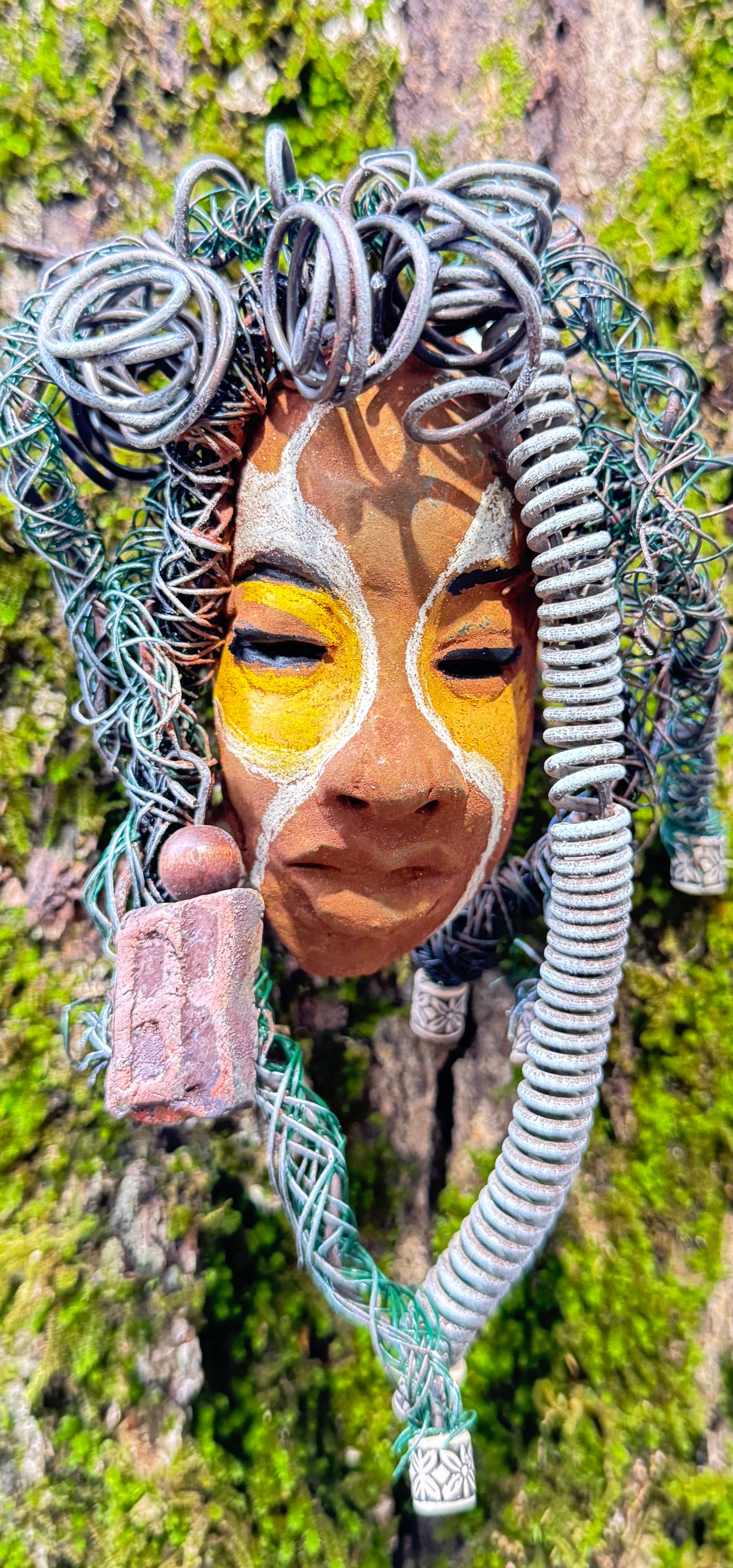 This eye-catching raku fired mask named Mitchell adds a unique touch to any collection, measuring 4” x 6” and weighing 6oz. It features 25 feet of 24 and 16 gauge wire and a three-colored complexion, all captured in stunning photography on a tree. To complete the look, the piece comes with two large Raku fired earrings with wooden beads. Don't hesitate to add Mitchell to your HerDew collection.