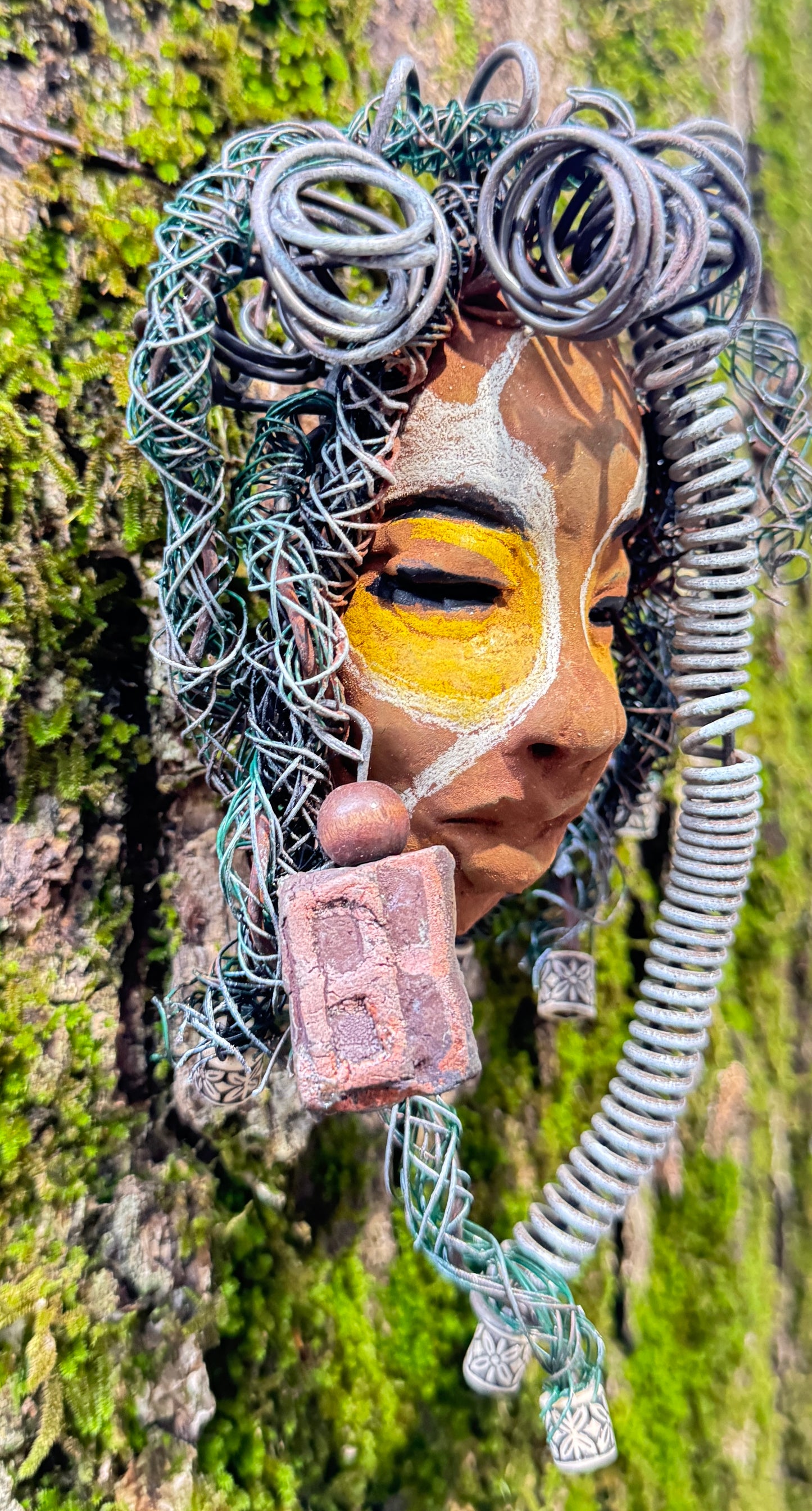 This eye-catching raku fired mask named Mitchell adds a unique touch to any collection, measuring 4” x 6” and weighing 6oz. It features 25 feet of 24 and 16 gauge wire and a three-colored complexion, all captured in stunning photography on a tree. To complete the look, the piece comes with two large Raku fired earrings with wooden beads. Don't hesitate to add Mitchell to your HerDew collection.