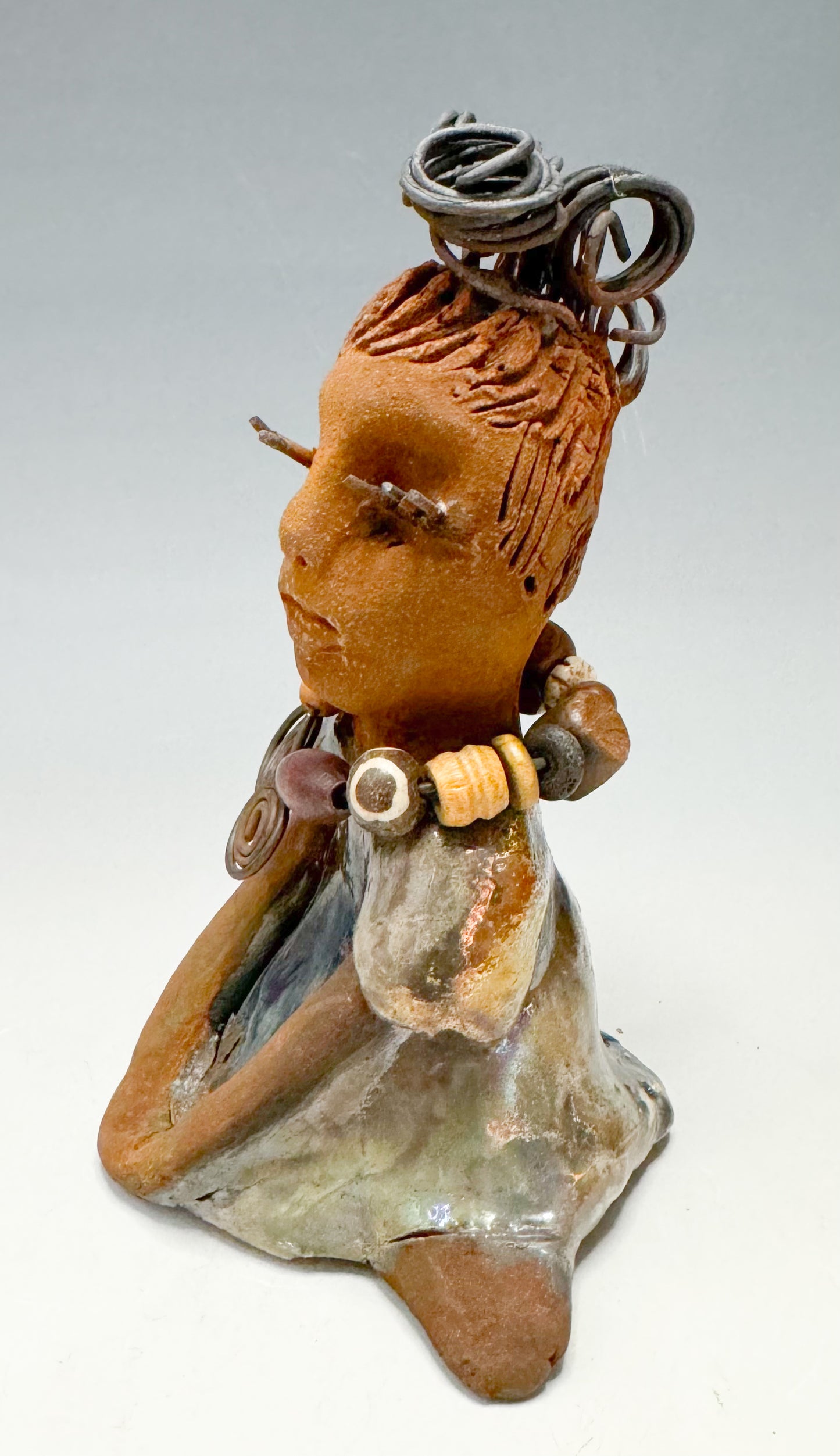 Introducing Kitty, the fearless one standing at 6" x 4" x 3" and weighing 12 ozs! Adorned in a stunning metallic gold dress, Kitty's coiled wire hair measures over 3 feet. Poised in a yoga pose, her long arms rest confidently at her lap. Start your collection off strong with the captivating Kitty from the Herdew Collection