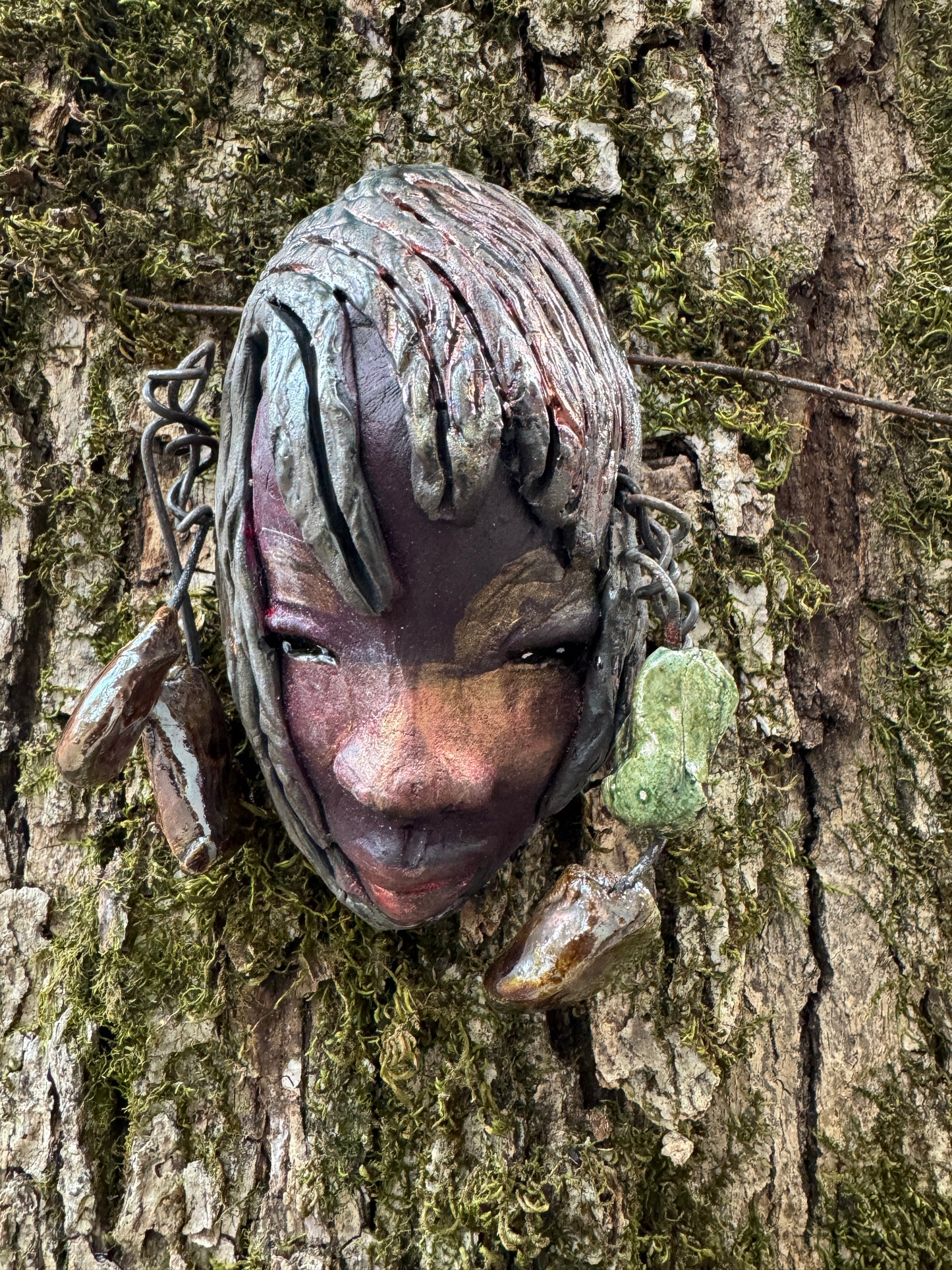 Monroe is 3" x 5" and weighs 5.5 oz. It is a Raku fired mask crafted from mixed media, with hand-crafted beads and 16 gauge wire used in its "hair". Whether inside or outdoors, it can be the perfect decoration for your home; the photo of Monroe was taken on a tree.
