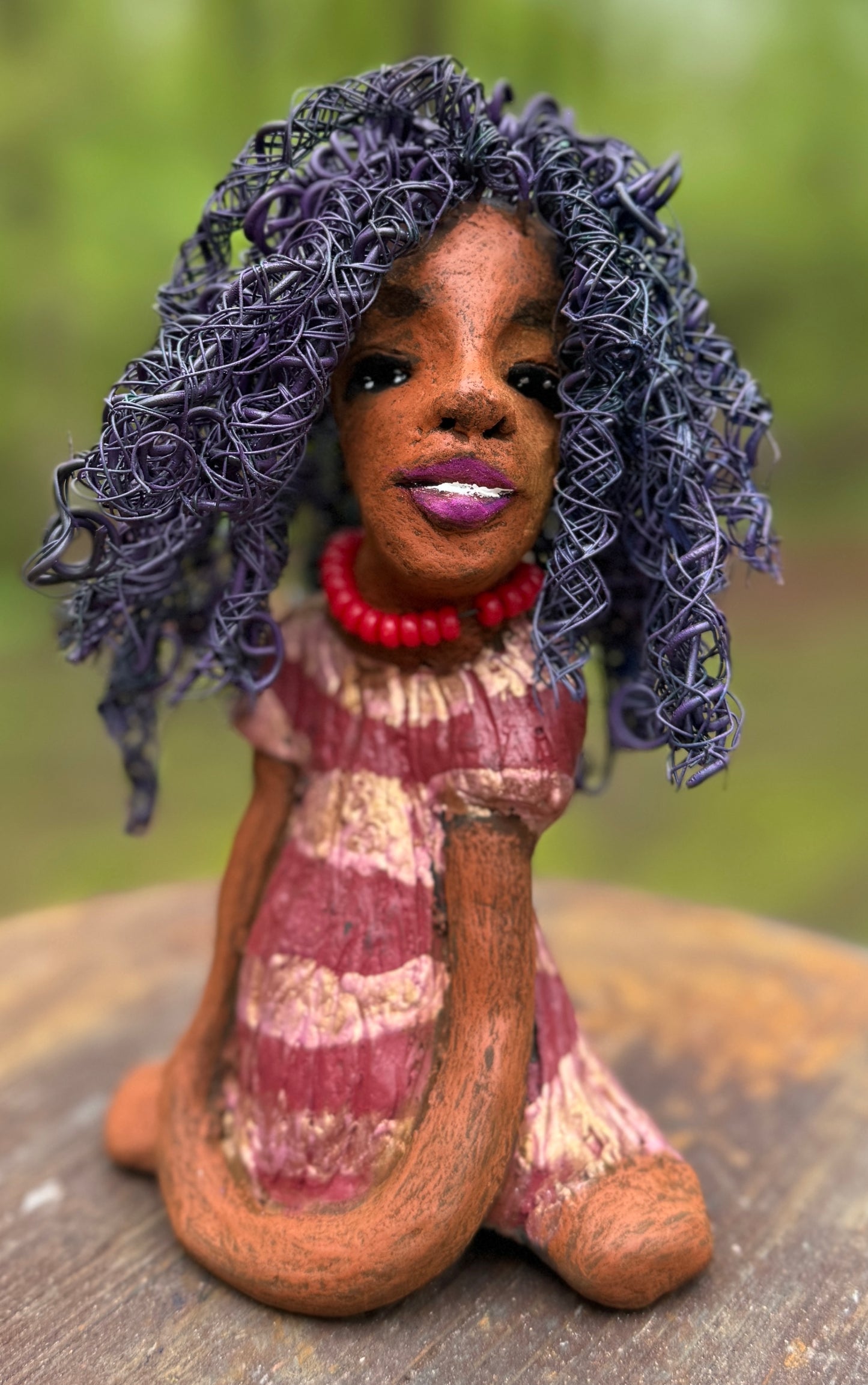 Introducing LaDonya, who measures 8" x 4. 5" x 5.5" and weighs 1.27 lbs. Her beauty is adorned with a lovely honey brown complexion, soft dark red lips, and long twisted purple locs that cascade down to her waist. Her metallic striped copper gold glazed dress adds a luxurious touch. With over 75 feet of 16 and 24 gauge wire for hair, it took over 6 hours to perfect her twisted hairstyle. Her hopeful expression and captivating eyes make her the perfect addition to any home. Plus, enjoy free shipping with our