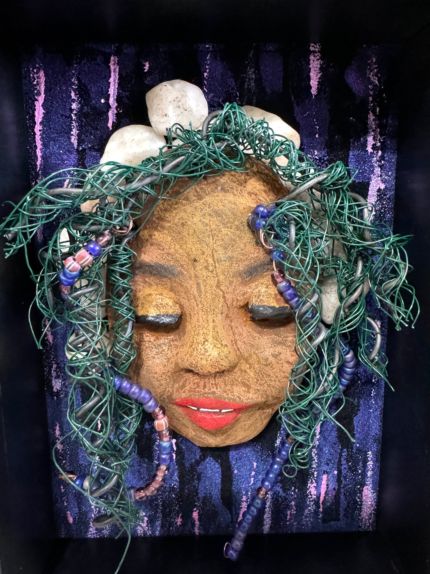 Presenting Shelby: A captivating mixed media sculpture made with a raku firing technique. Meticulously crafted features include a unique two-tone honey brown complexion, subtle Ruby red lips, and hair intricately woven with 16 and 24 gauge wire. This piece is mounted on a hand-painted canvas, featuring a beautifully landscaped background, and elegantly displayed in a glass covered 5" x 7" black shadowbox.