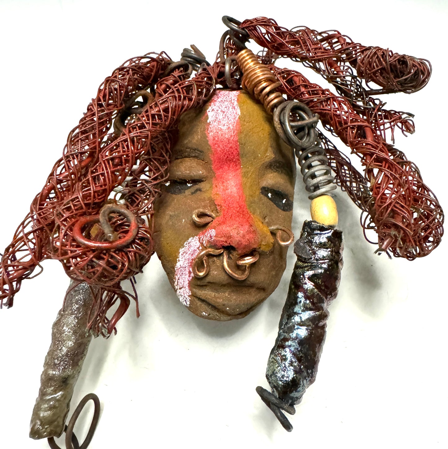 Billy is a 5" x 7" Raku-fired mask with intricate detail. Constructed with 16 and 24-gauge wire, spanning a total of 20 feet, he features a two tone, honey brown and red stripe complexion, matched with vibrant red coiled locs. Now available at a discount, Billy is an ideal choice for collectors or as a special holiday surprise.