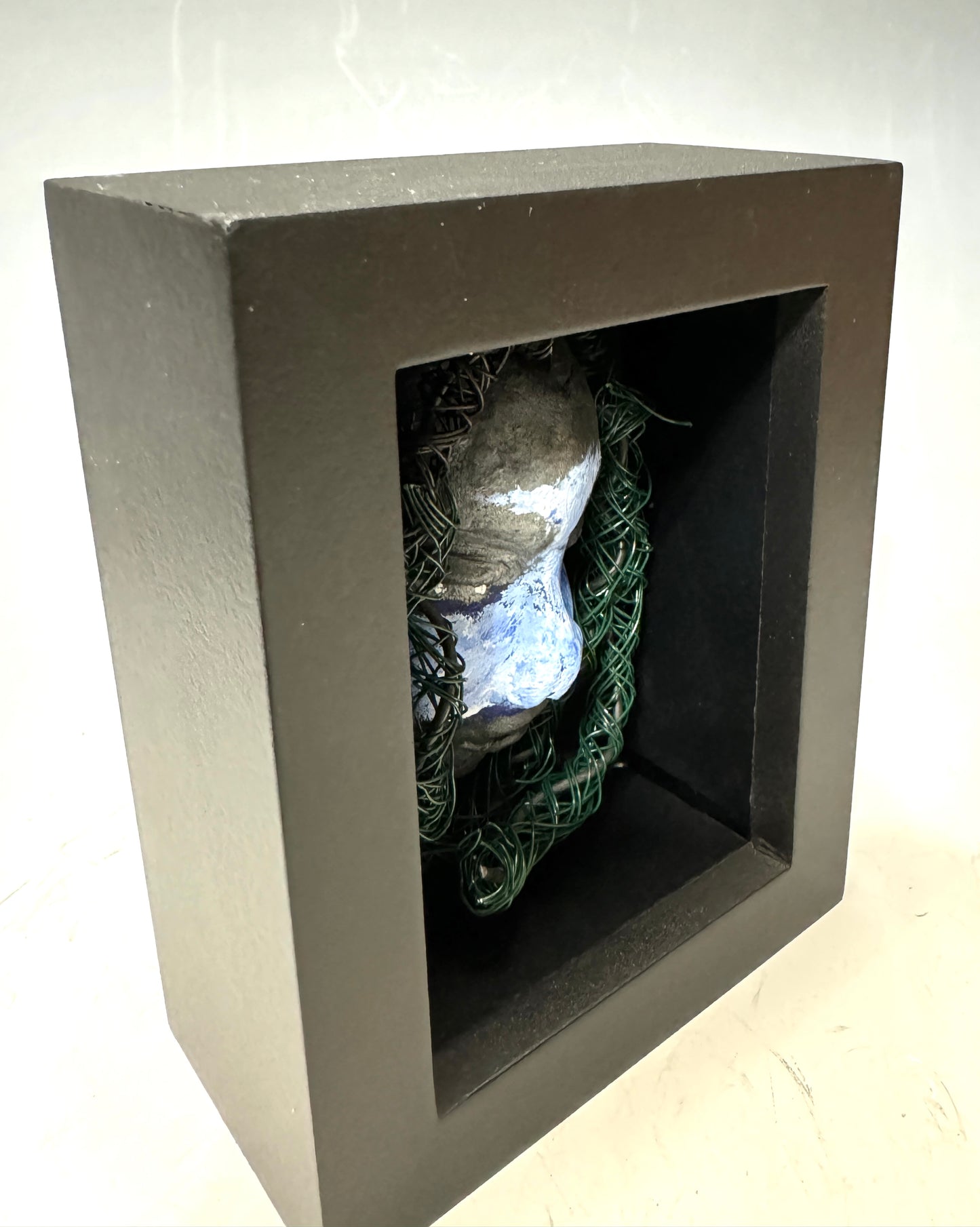 Chandon is a raku fired mask .He is enclosed in a 4“ x 4“ glass covered black shadowbox. He has over 40 feet of 16 and 24 gauge wire as hair. Make a bold statement with this striking mask! Enclosed in a sleek glass shadowbox, Chandon features a unique raku firing technique that makes each creation one-of-a-kind. The wire "hair" extends over 40 feet in length, representing a spirit that is free to explore and take risks. Bring a touch of adventure into your home with this handcrafted piece.