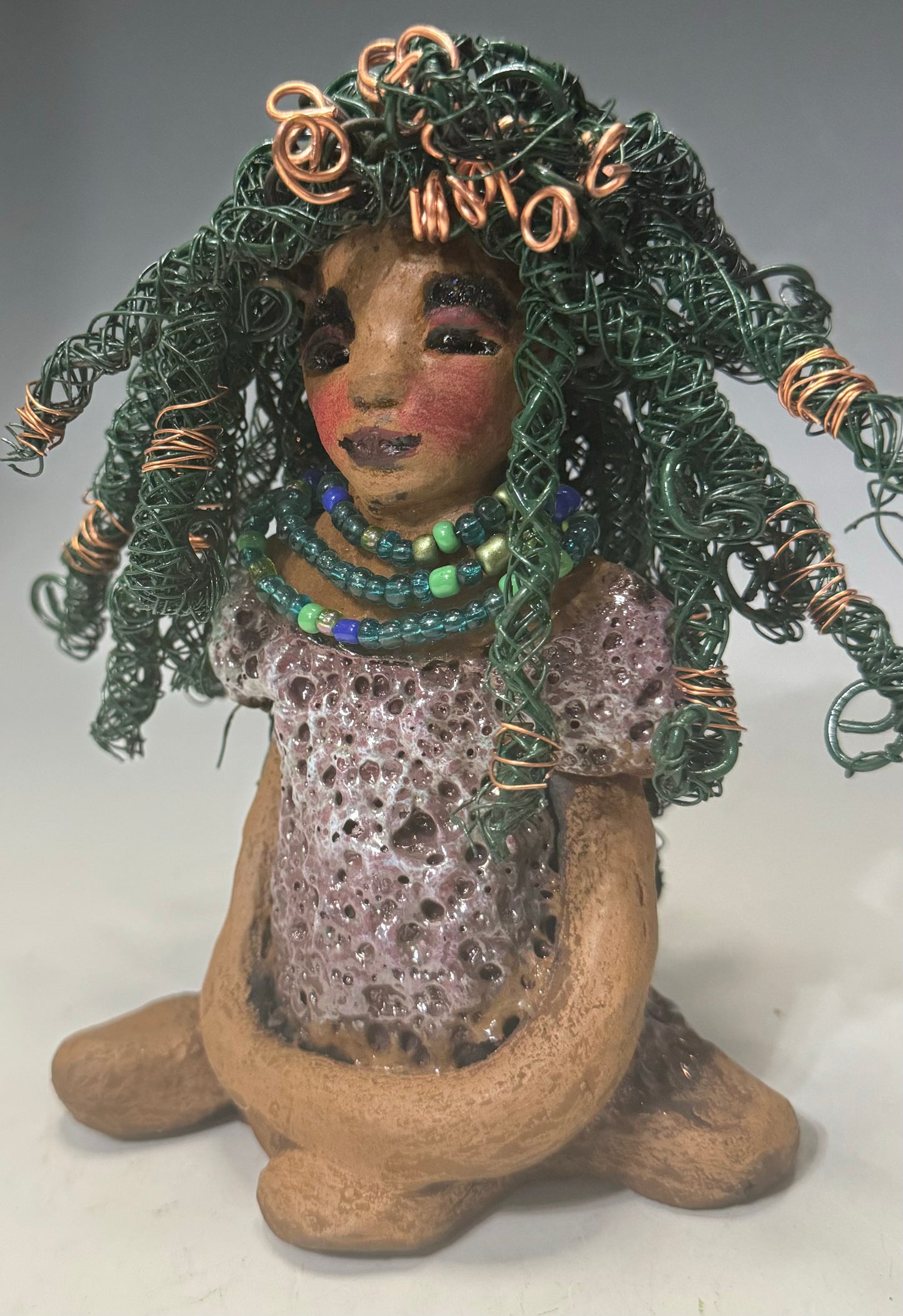 Say Hello to Layla – a sophisticated 6" x 5" x 4" statue standing at 1.03 lbs. with a honey brown complexion and reddish brown lips. She proudly wears a green and copper wire hairstyle. Layla wears a metallic copper glazed dress, plus a beaded blue and green necklace. With eyes wide open, Layla is eager to join her new home. Have questions? Chat with us and enjoy free shipping when you purchase her!