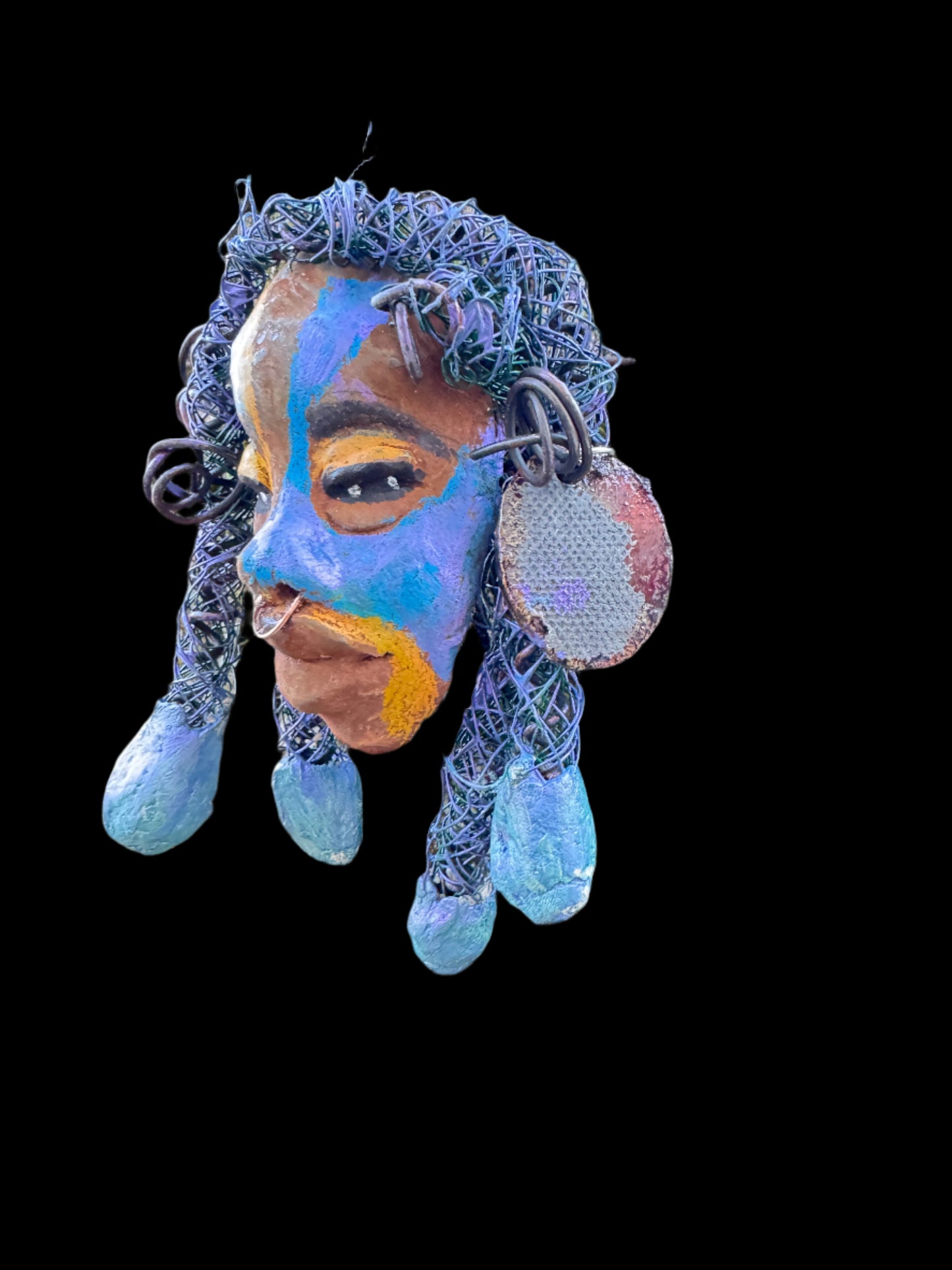 Esi is a lightweight 4 x 6" mixed media raku fire mask that combines a striking design with 24 and 16 gauge wire, 5 intricate blue tribal beads, and over 15 feet of wire. It can be proudly displayed against a solid black or white background, or for an even more impressive effect, consider a backdrop featuring lush, mossy trees.