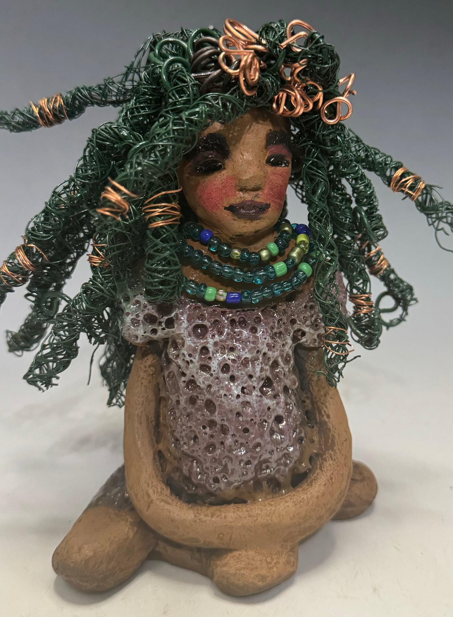 Say Hello to Layla – a sophisticated 6" x 5" x 4" statue standing at 1.03 lbs. with a honey brown complexion and reddish brown lips. She proudly wears a green and copper wire hairstyle. Layla wears a metallic copper glazed dress, plus a beaded blue and green necklace. With eyes wide open, Layla is eager to join her new home. Have questions? Chat with us and enjoy free shipping when you purchase her!