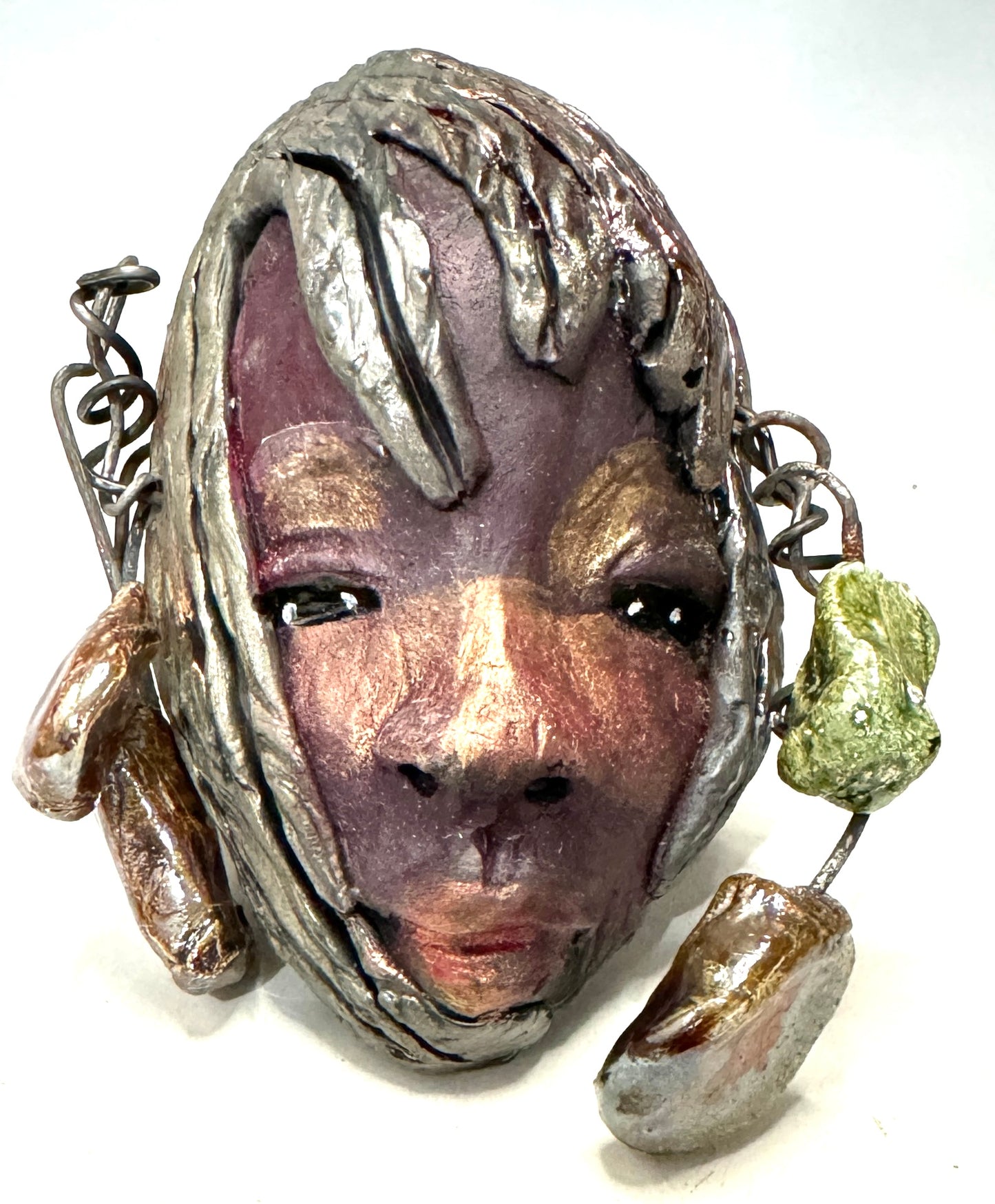 Monroe is 3" x 5" and weighs 5.5 oz. It is a Raku fired mask crafted from mixed media, with hand-crafted beads and 16 gauge wire used in its "hair". Whether inside or outdoors, it can be the perfect decoration for your home; the photo of Monroe was taken on a tree.