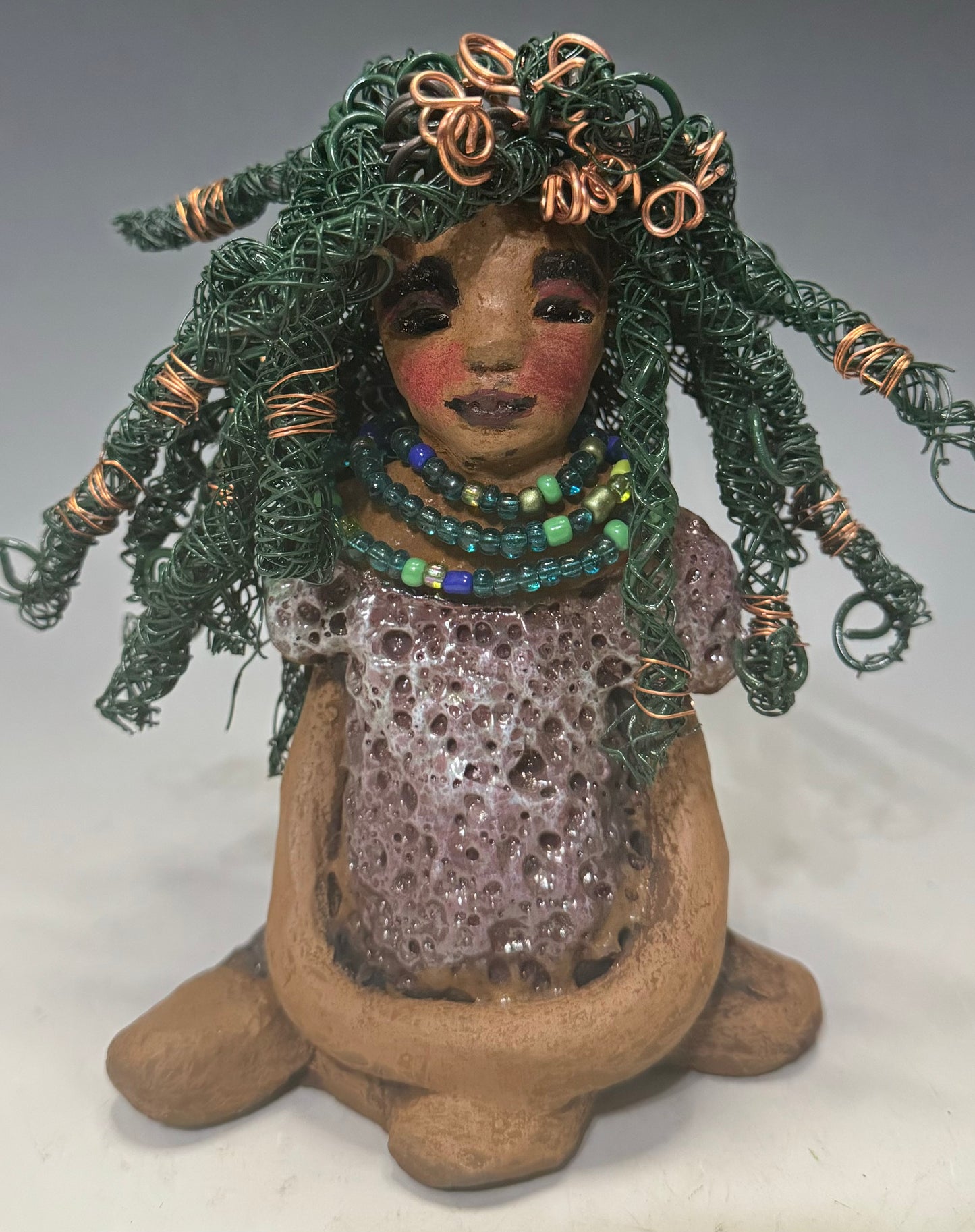 Say Hello to Layla – a sophisticated 6" x 5" x 4" statue standing at 1.03 lbs. with a honey brown complexion and reddish brown lips. She proudly wears a green and copper wire hairstyle. Layla wears a metallic copper glazed dress, plus a beaded blue and green necklace. With eyes wide open, Layla is eager to join her new home. Have questions? Chat with us and enjoy free shipping when you purchase her!