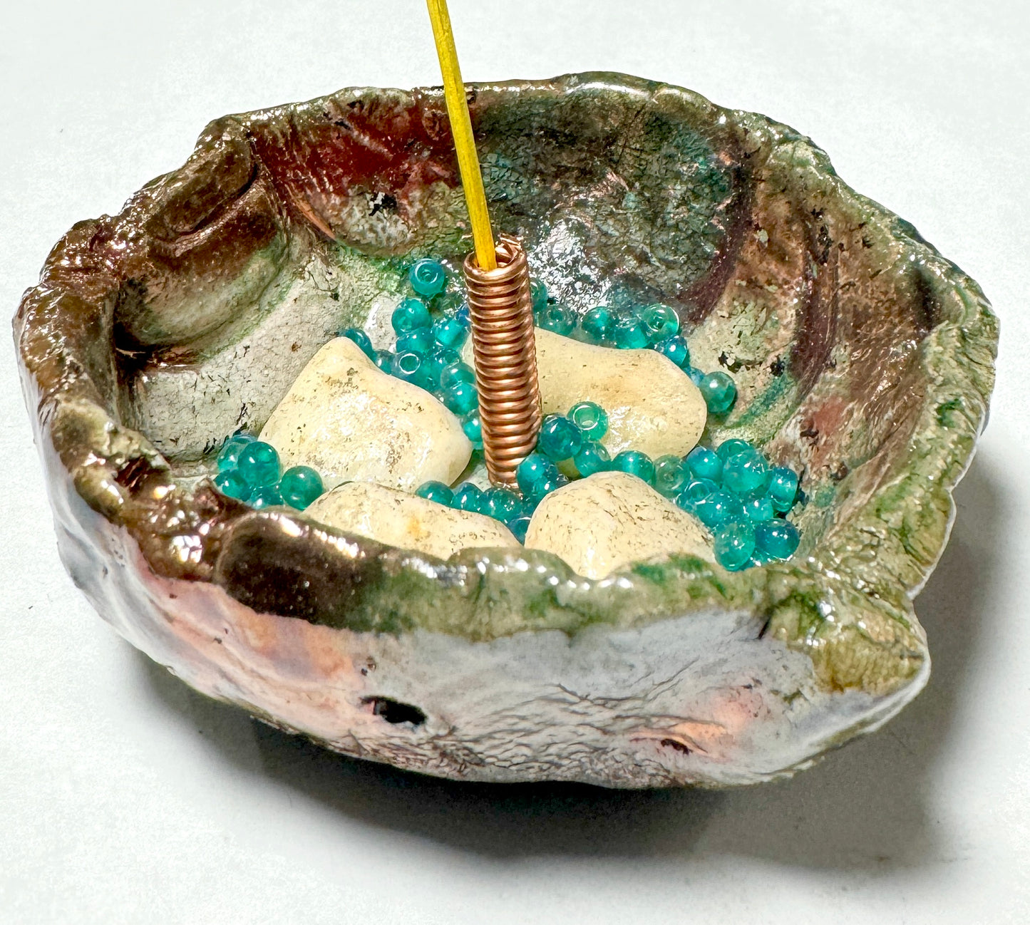 This 1" x 3" x 3" incense holder has been expertly crafted with earthy off-white stones and aqua blue beads and coated in a copper high gloss Raku glaze.