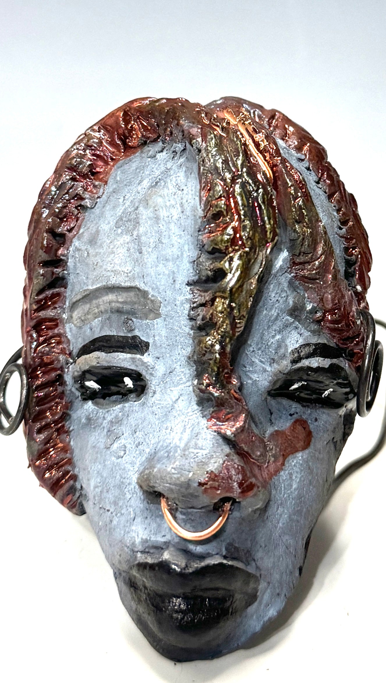 Tia weighs 3.2 oz and measures 4" by 3" in diameter. Her hair is copper-braided and her complexion is a light grayish blue hue with black lips. She is an ideal introductory piece from the HerDew mask collection.