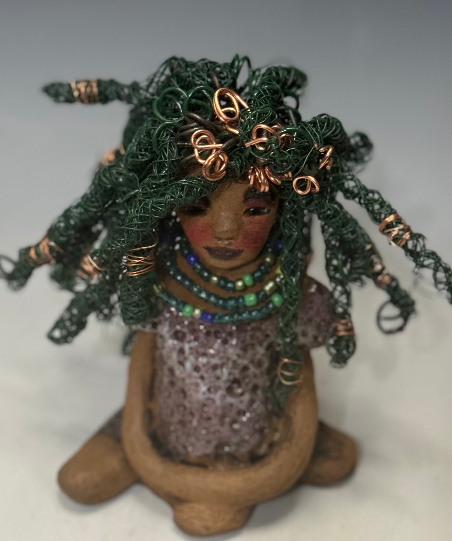 Say Hello to Layla – a sophisticated 6" x 5" x 4" statue standing at 1.03 lbs. with a honey brown complexion and reddish brown lips. She proudly wears a green and copper wire hairstyle. Layla wears a metallic copper glazed dress, plus a beaded blue and green necklace. With eyes wide open, Layla is eager to join her new home. Have questions? Chat with us and enjoy free shipping when you purchase her!