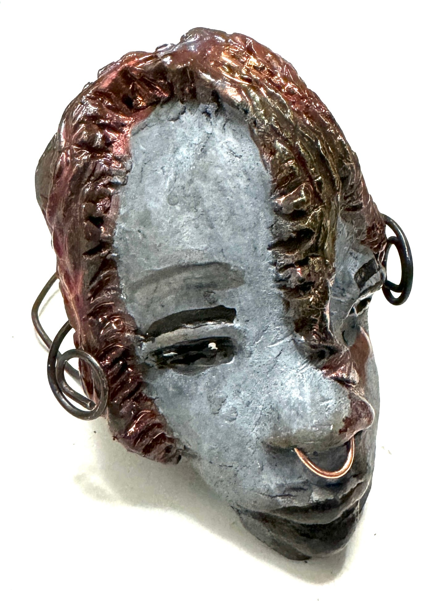 Tia weighs 3.2 oz and measures 4" by 3" in diameter. Her hair is copper-braided and her complexion is a light grayish blue hue with black lips. She is an ideal introductory piece from the HerDew mask collection.