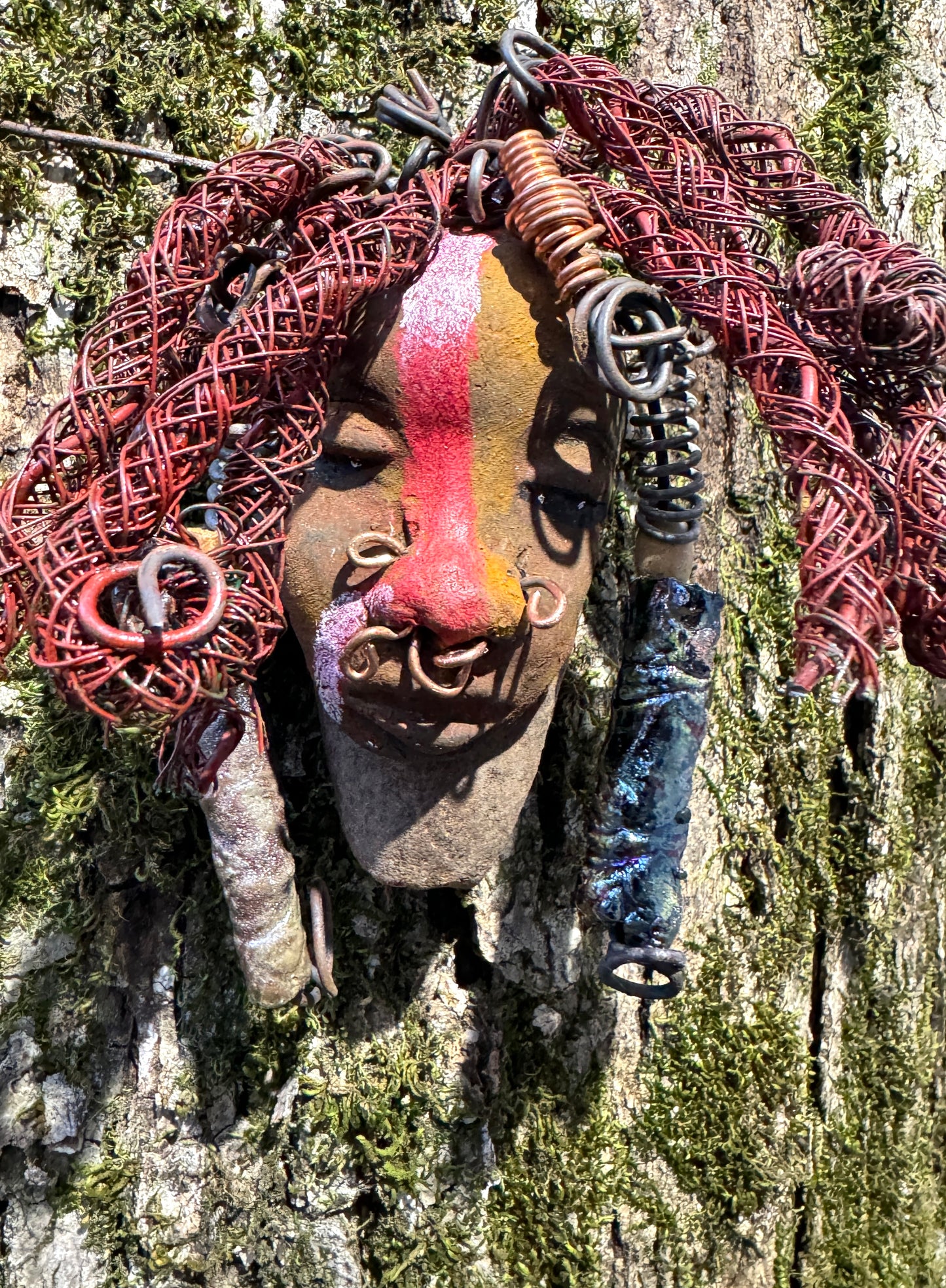 Billy is a 5" x 7" Raku-fired mask with intricate detail. Constructed with 16 and 24-gauge wire, spanning a total of 20 feet, he features a two tone, honey brown and red stripe complexion, matched with vibrant red coiled locs. Now available at a discount, Billy is an ideal choice for collectors or as a special holiday surprise.