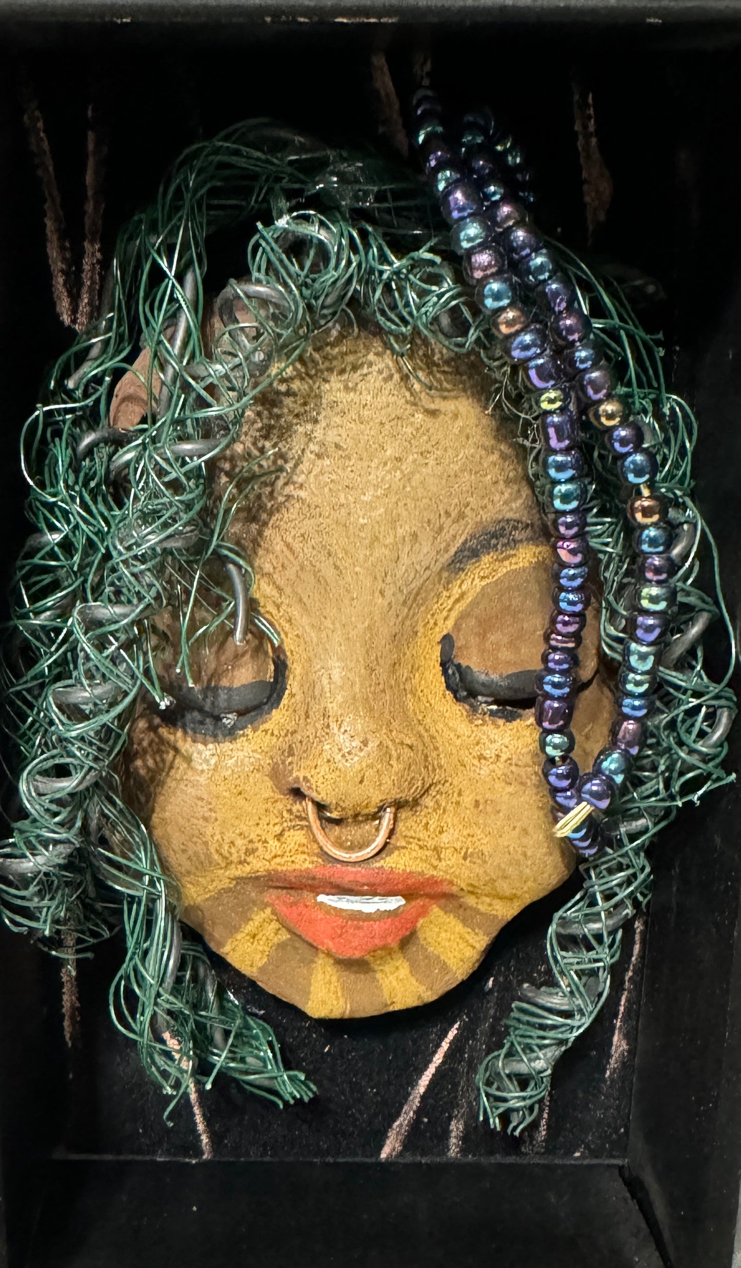 ntroducing Baraka: An alluring mixed media sculpture created using the raku firing method. Impeccably designed attributes include a distinctive dual-toned honey brown complexion, delicate Ruby red lips, and intricately woven hair using 16 and 24 gauge wire. Mounted on a hand-painted canvas with a stunning landscape backdrop, this piece is elegantly showcased in a 5" x 7" black shadowbox, protected by a glass cover.