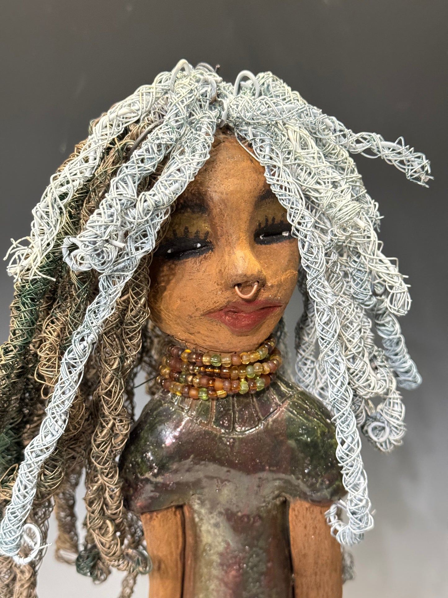 At 15" x 5" x 5" and weighing 3.1lbs, Tia is a large figure with detailed customizations. Her beige and honey brown complexion complements the 16 and 24 gauge white and gold wire hair on her head. She's outfitted in an alligator green metallic dress with shimmering copper accents that make her stand out from the crowd. Her enigmatic gaze is sure to draw people in. Free Shipping!