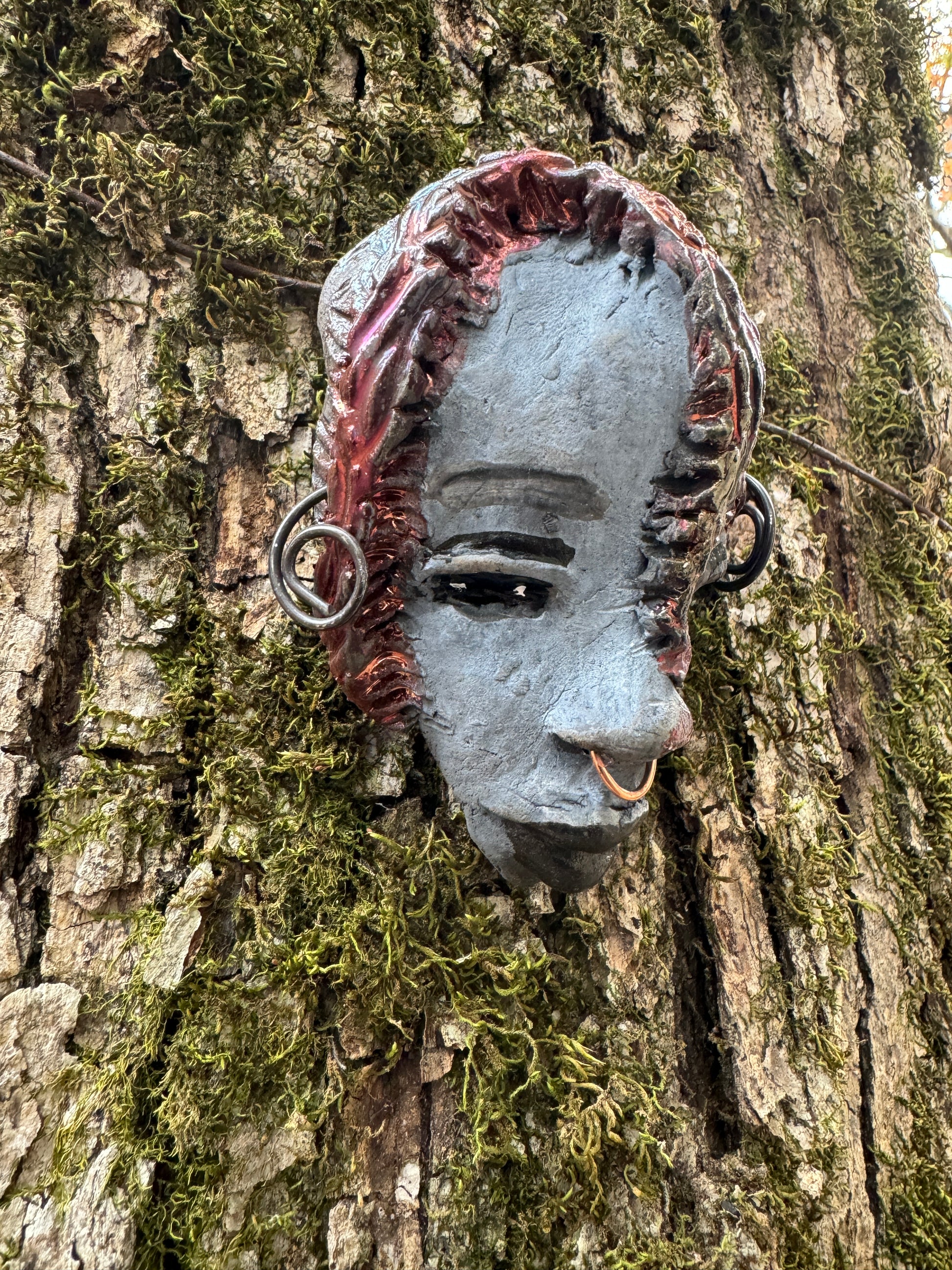Tia weighs 3.2 oz and measures 4" by 3" in diameter. Her hair is copper-braided and her complexion is a light grayish blue hue with black lips. She is an ideal introductory piece from the HerDew mask collection.