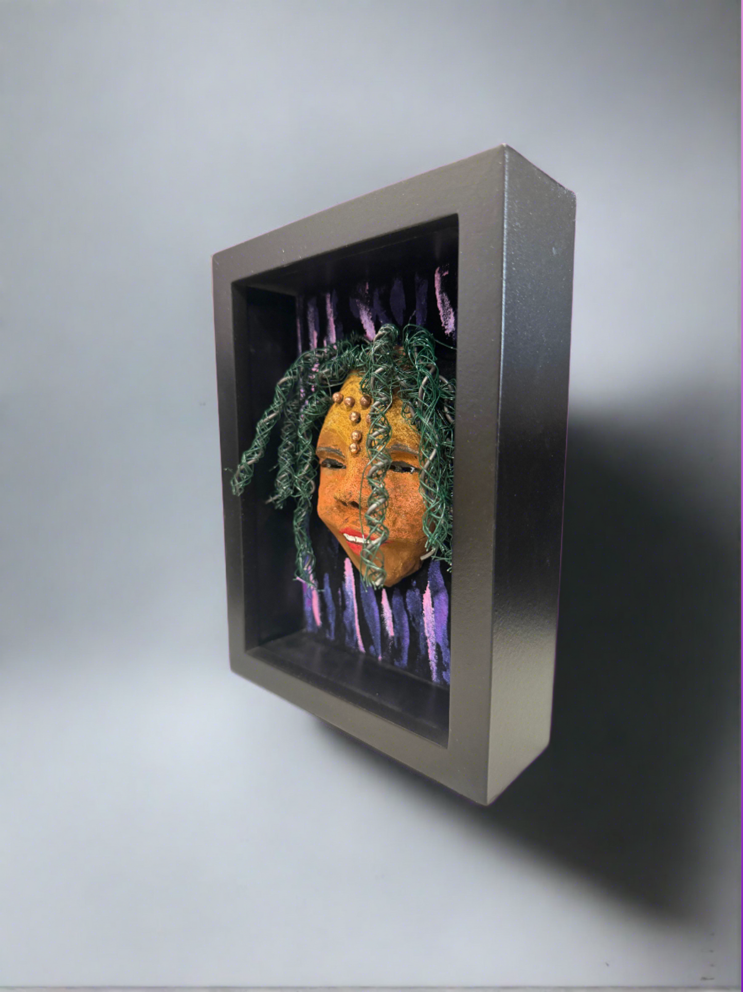 Kenti is a 5"x 7" raku mask displayed in a glass covered black shadowbox, accented with a beautiful two-tone honey brown complexion. Her intricate hair, made of 16 and 24 gauge wire and beads measures over 50 feet in length. With a contagious smile, Kenti adds a touch of elegance to any home decor.