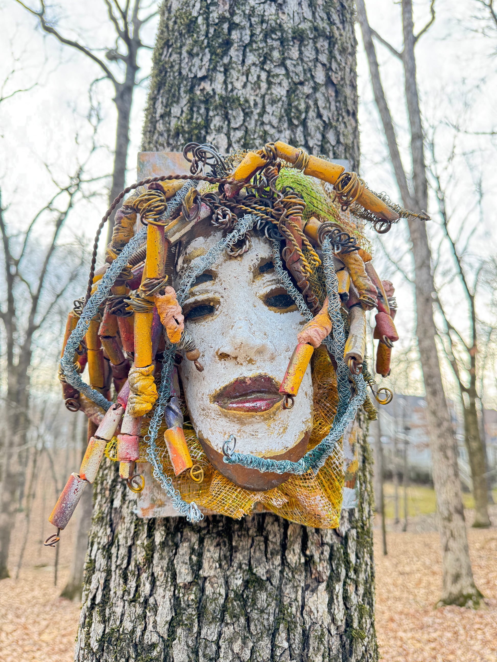 Experience the unique beauty of Amos, a mixed media raku fire mask carefully crafted with over 50 handmade beads and 50 feet of 24 and 16 gauge wire. Mounted on a 7” x 12” wood board and weighing approximately 4 pounds, Amos features an off-white face with braided and beaded  hair. This one-of-a-kind masterpiece also includes several fabrics of netting in his hair, making it larger than most masks.